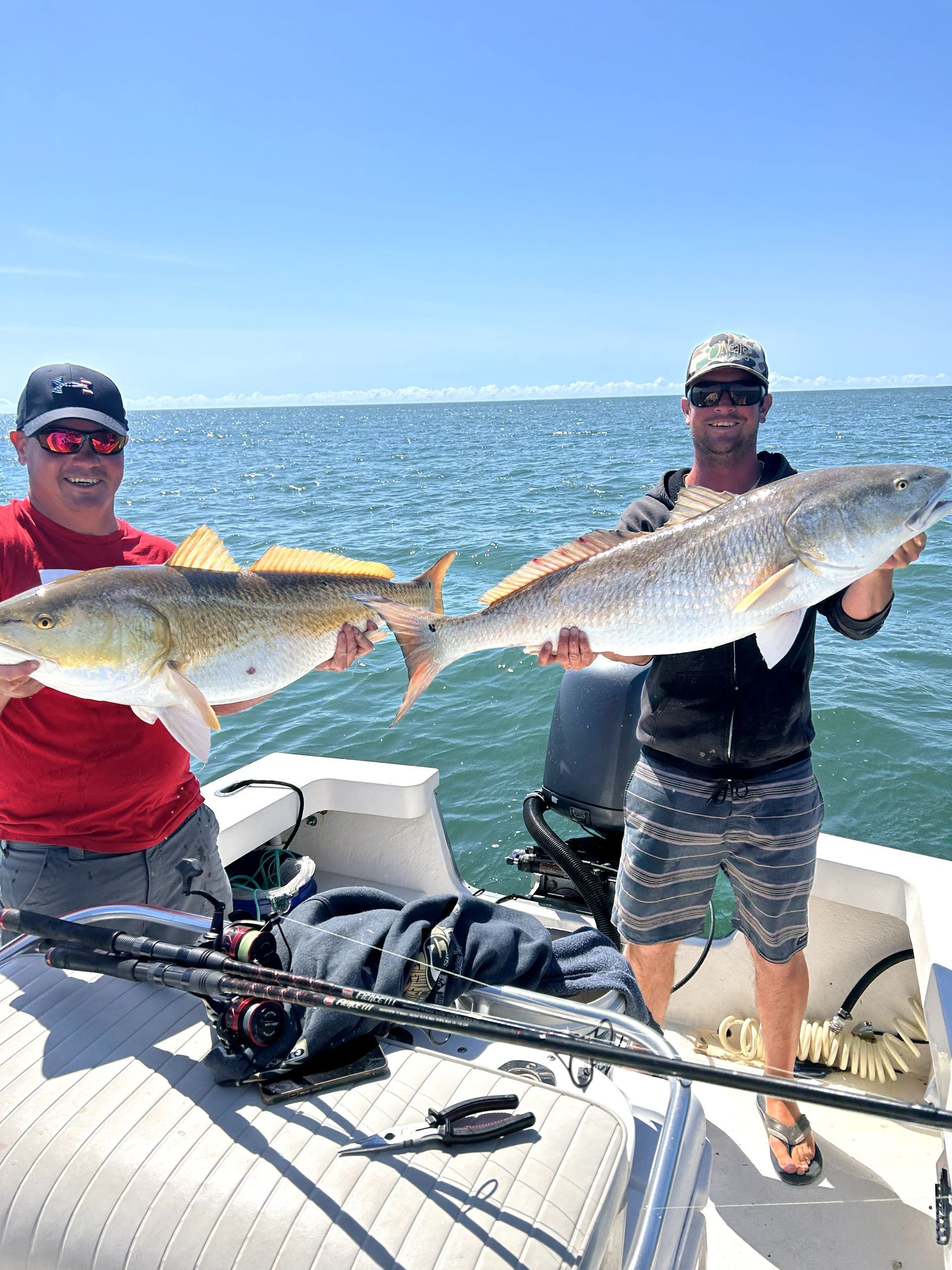 Two anglers on a boat holding large fish with open water and blue sky in the background