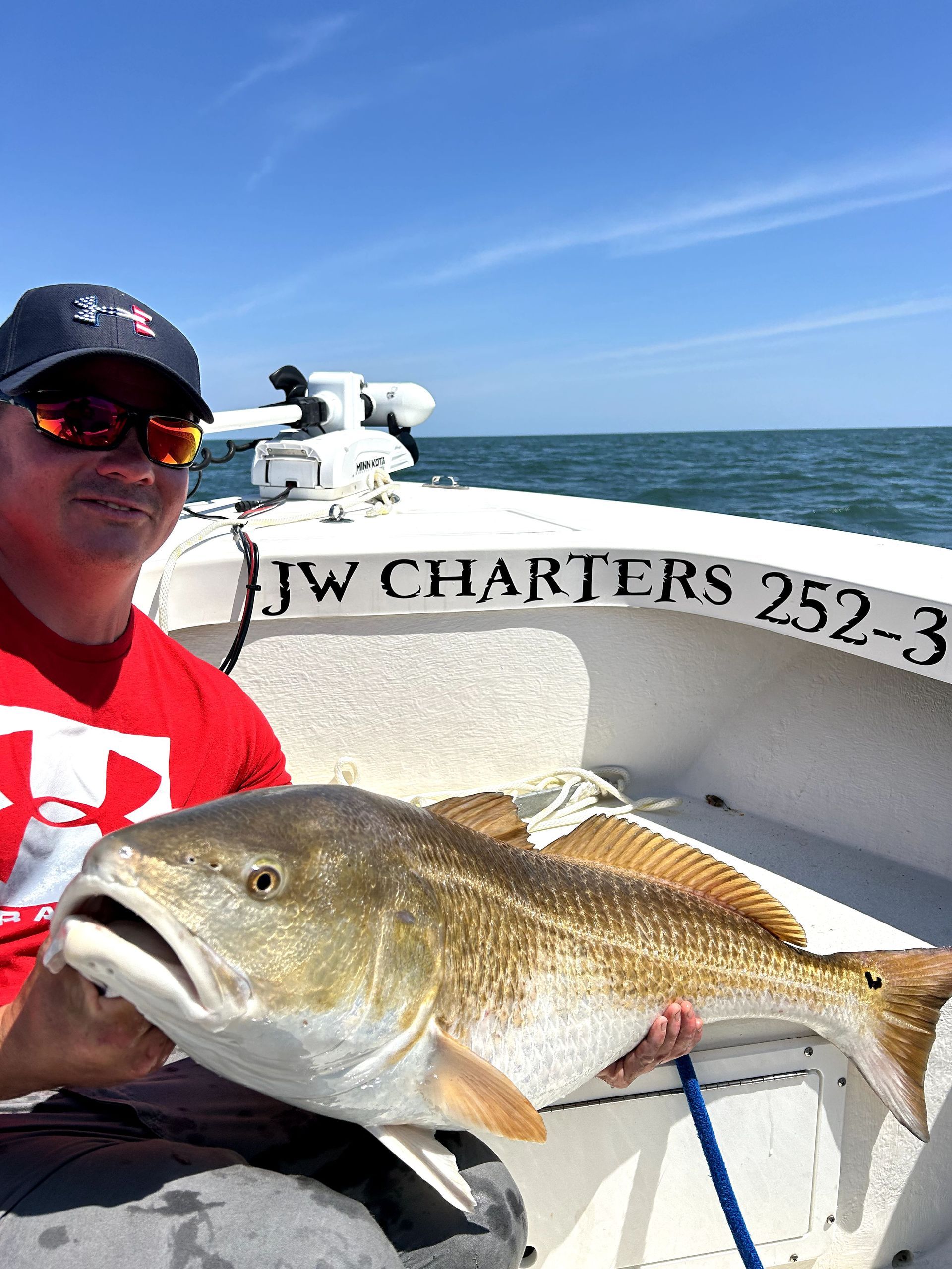 Man holding a large fish on a boat with ocean and blue sky in the background