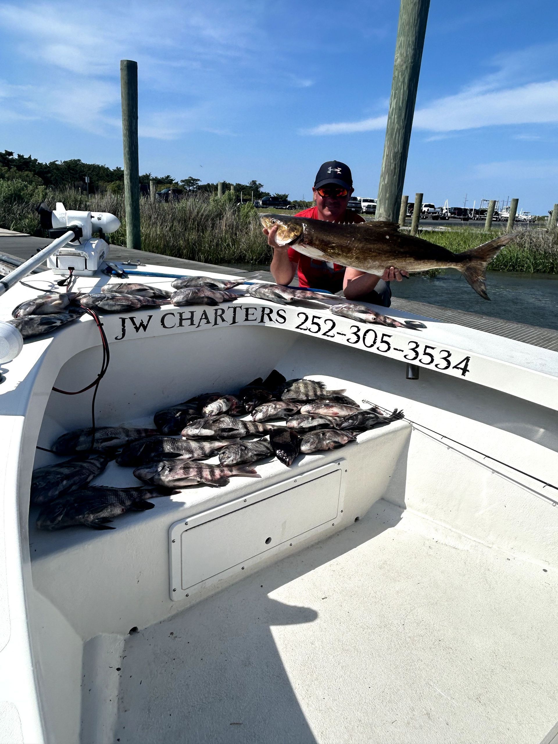 Two people on a boat with a pile of fish and a fishing charter sign at sea