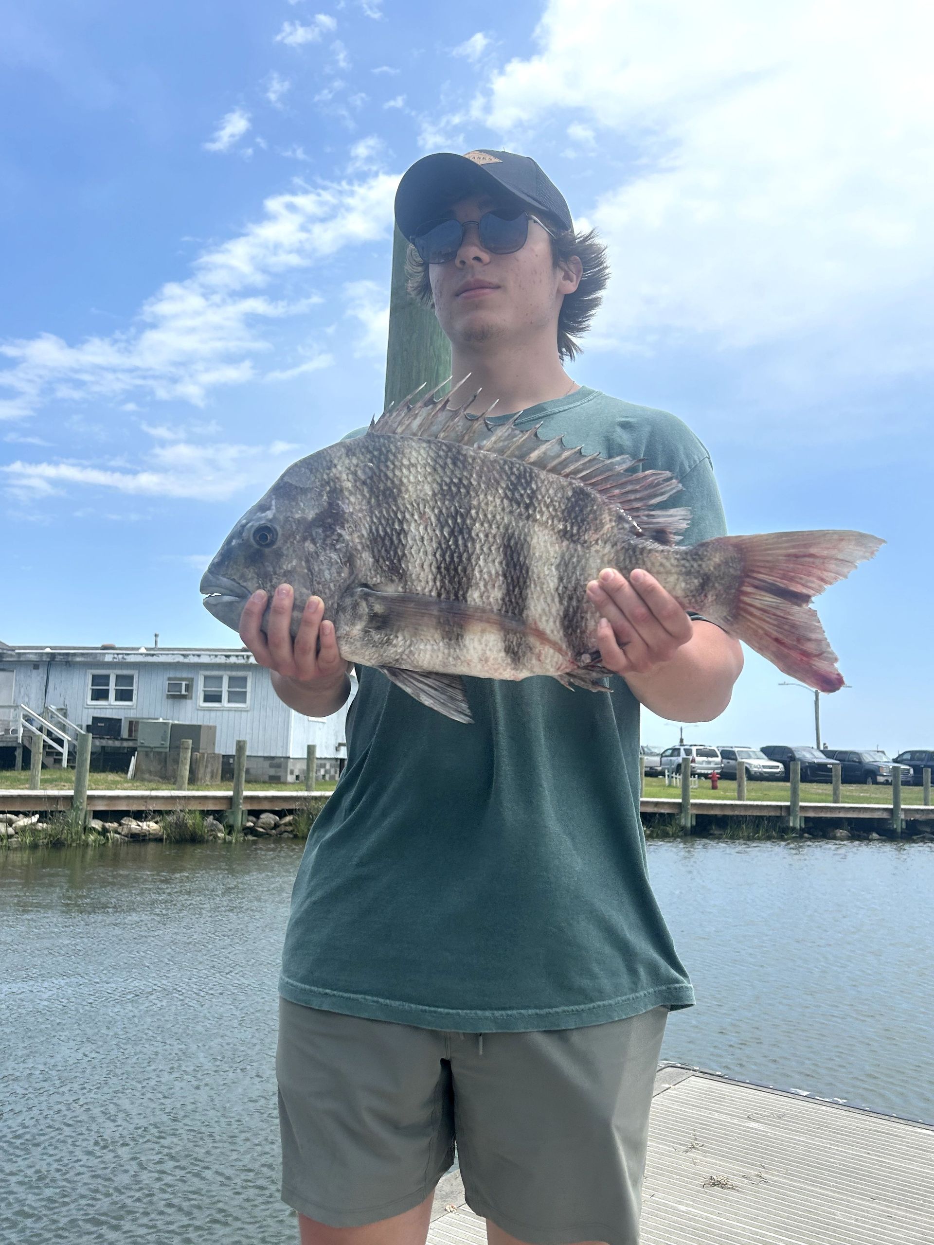 Person holding a large striped fish at a marina under a cloudy sky