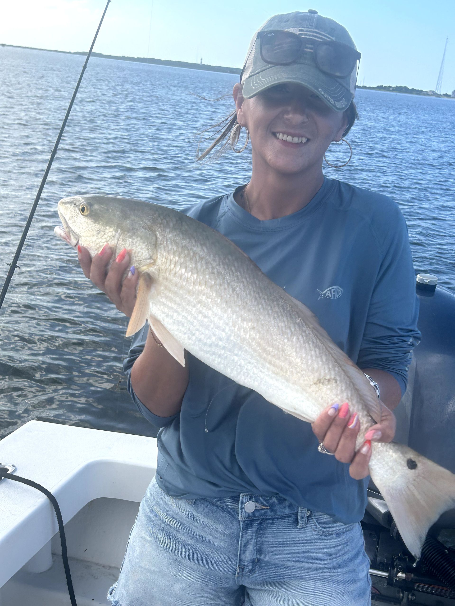 Smiling angler holding a large fish on a boat, with open water in the background