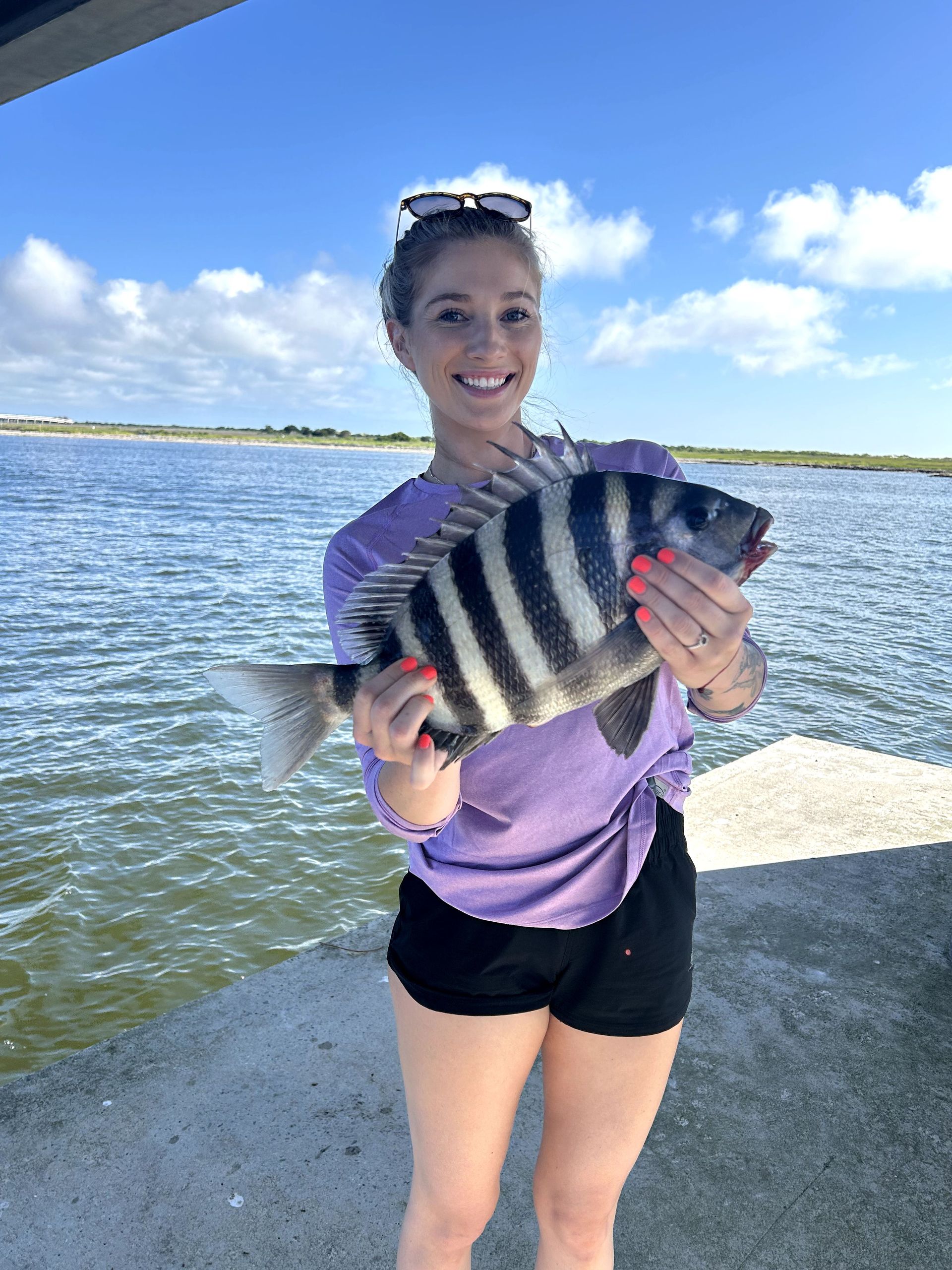 Person holding a striped fish on a sunny dock by the water