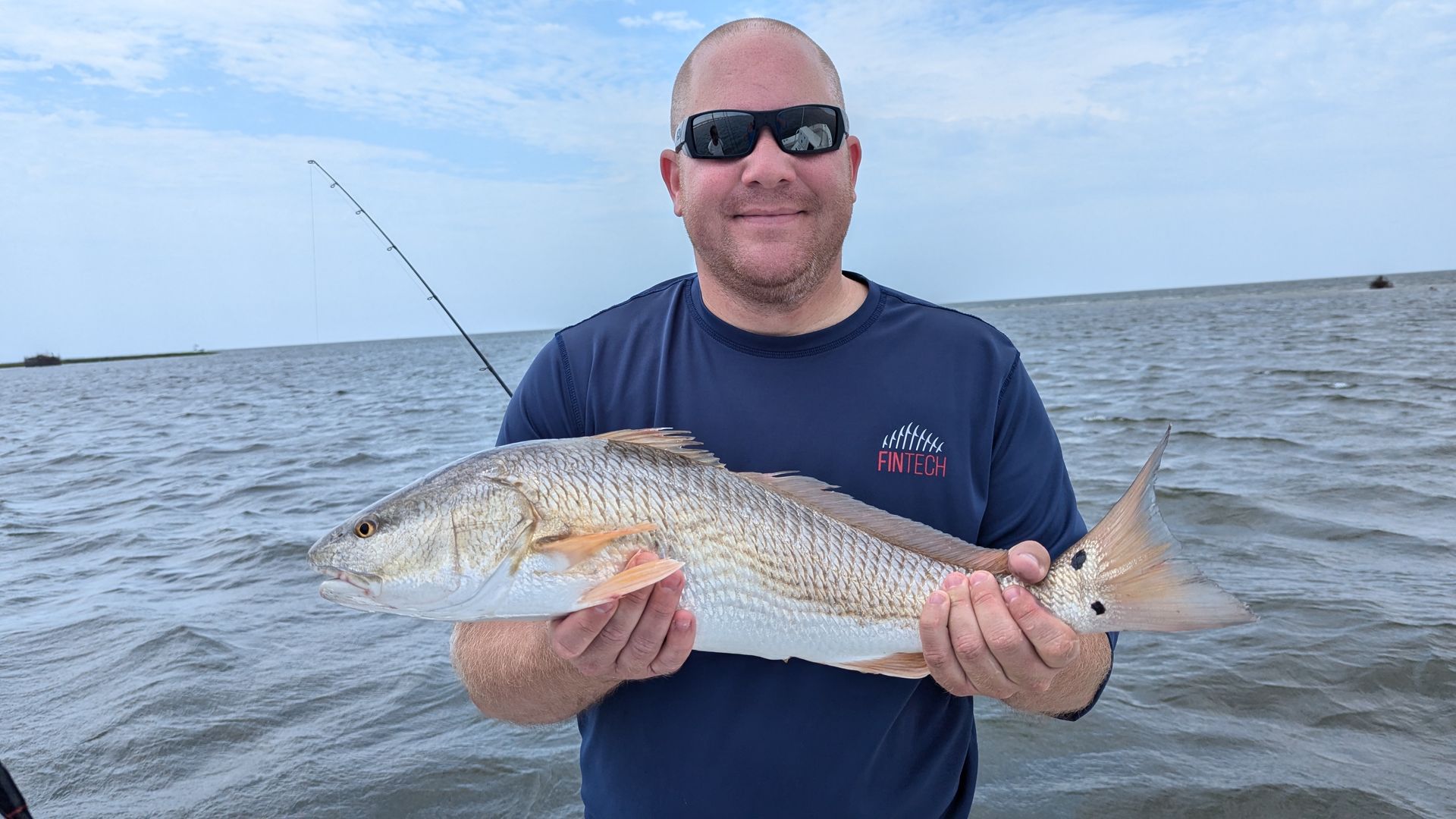 Man holding a large fish on a boat with open water in the background