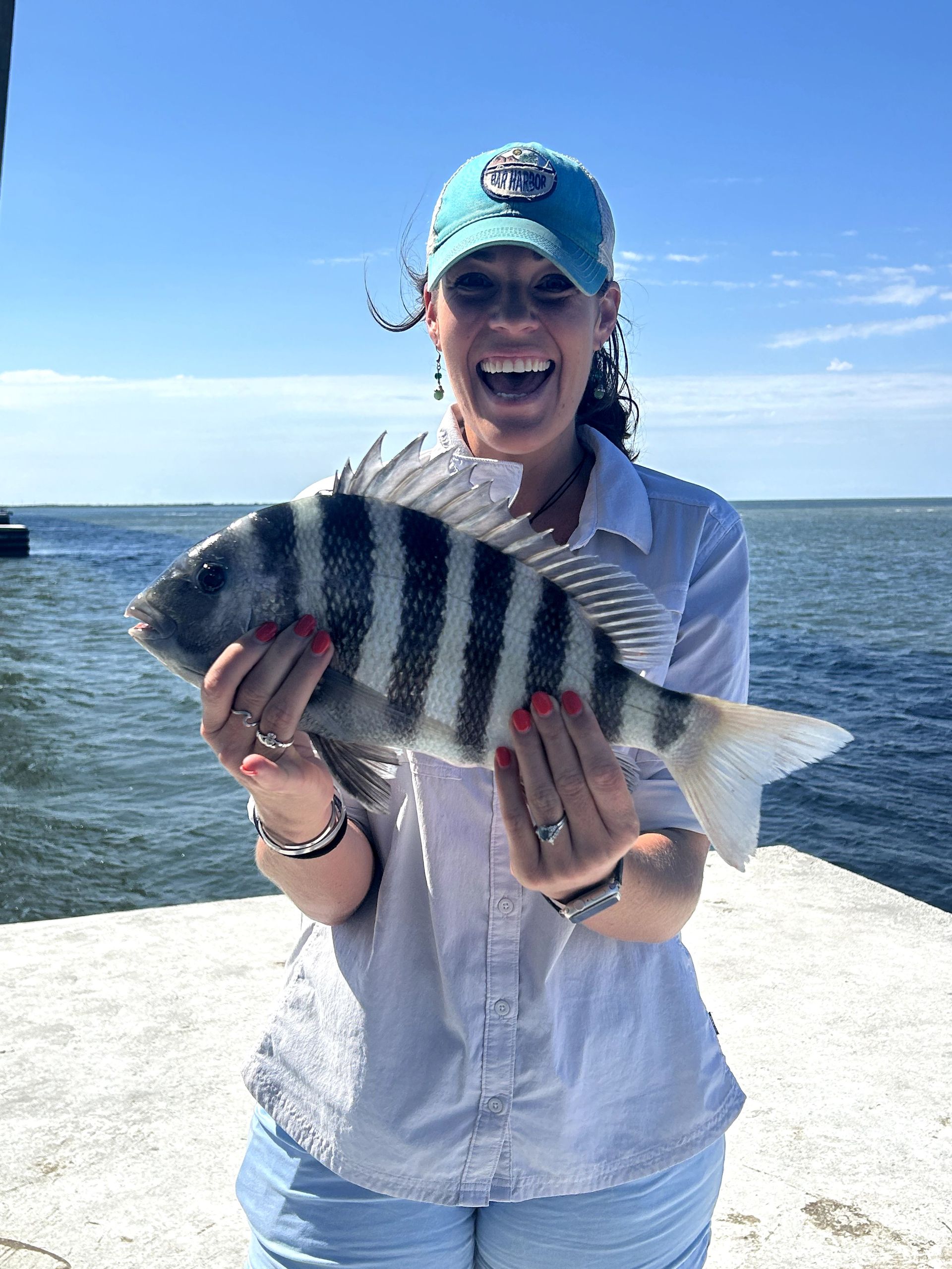 Person on a boat holds a striped fish and smiles under a blue sky.