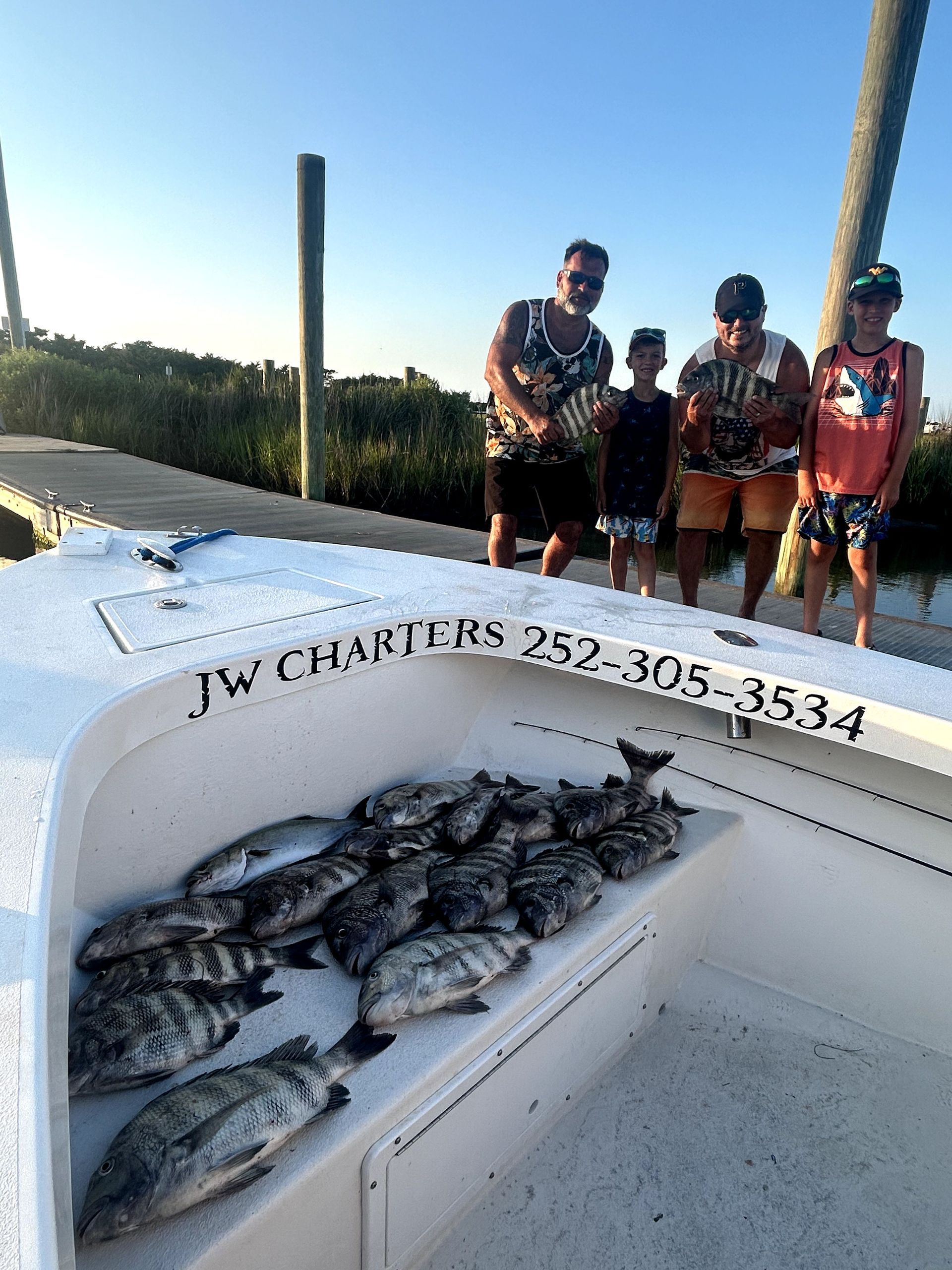 Three people on a boat with a large pile of fish in the bow at sunset