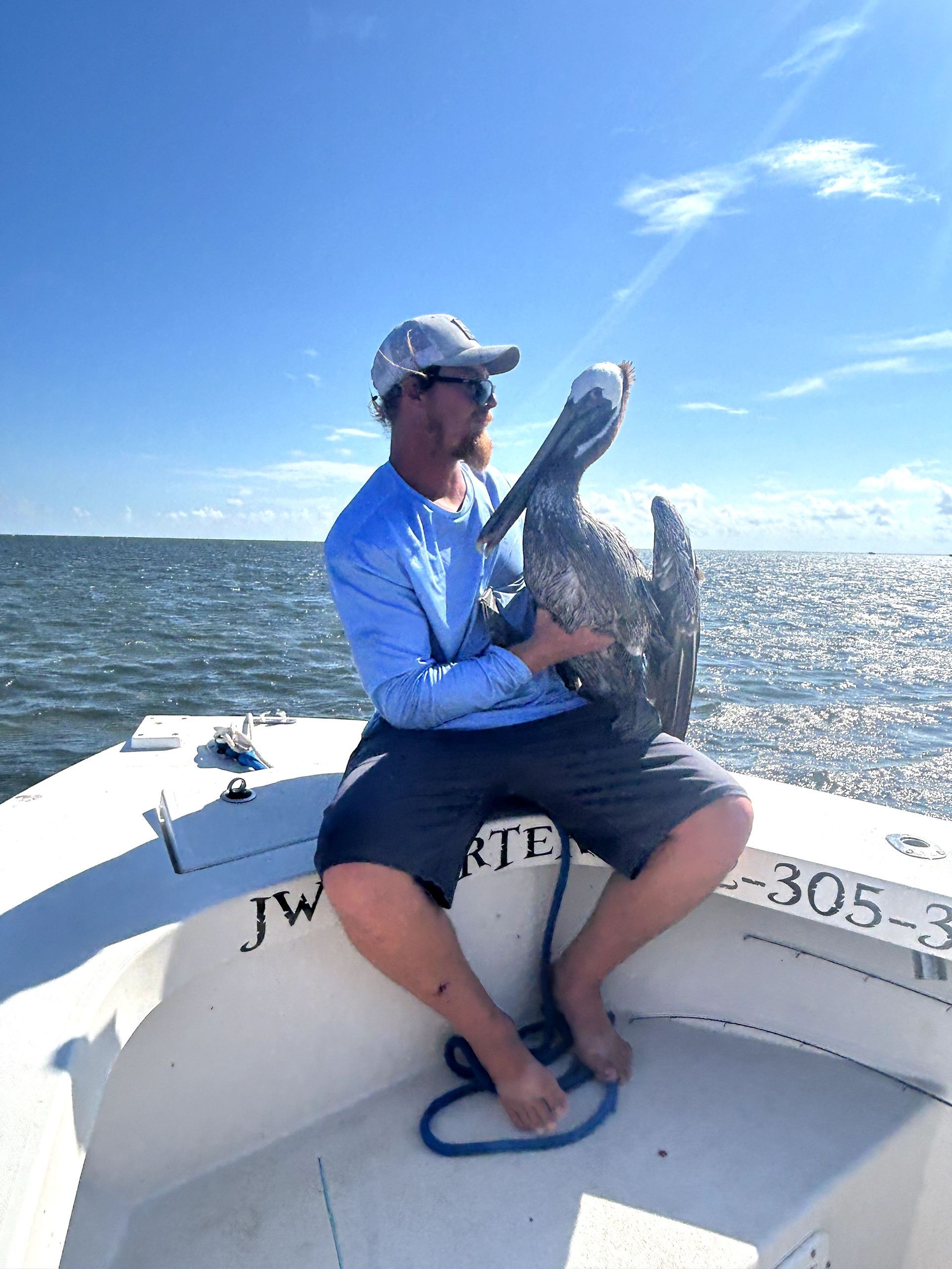 Man on a boat holding a large fish on open water under a blue sky.