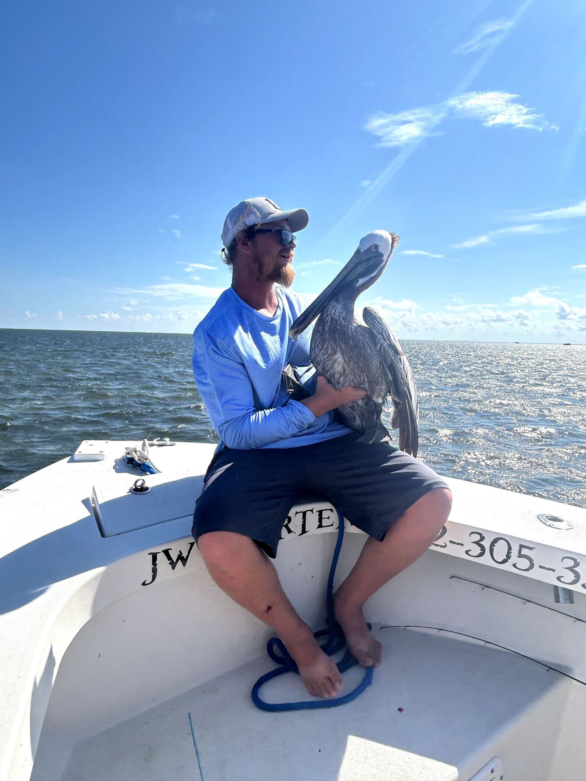Man seated on a boat holding a large fish on a sunny day with open water behind him