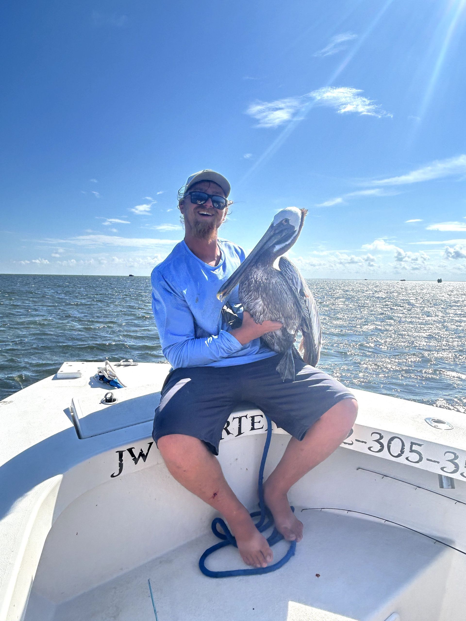 Man sitting on a boat holding a large fish on a sunny, windy day on open water