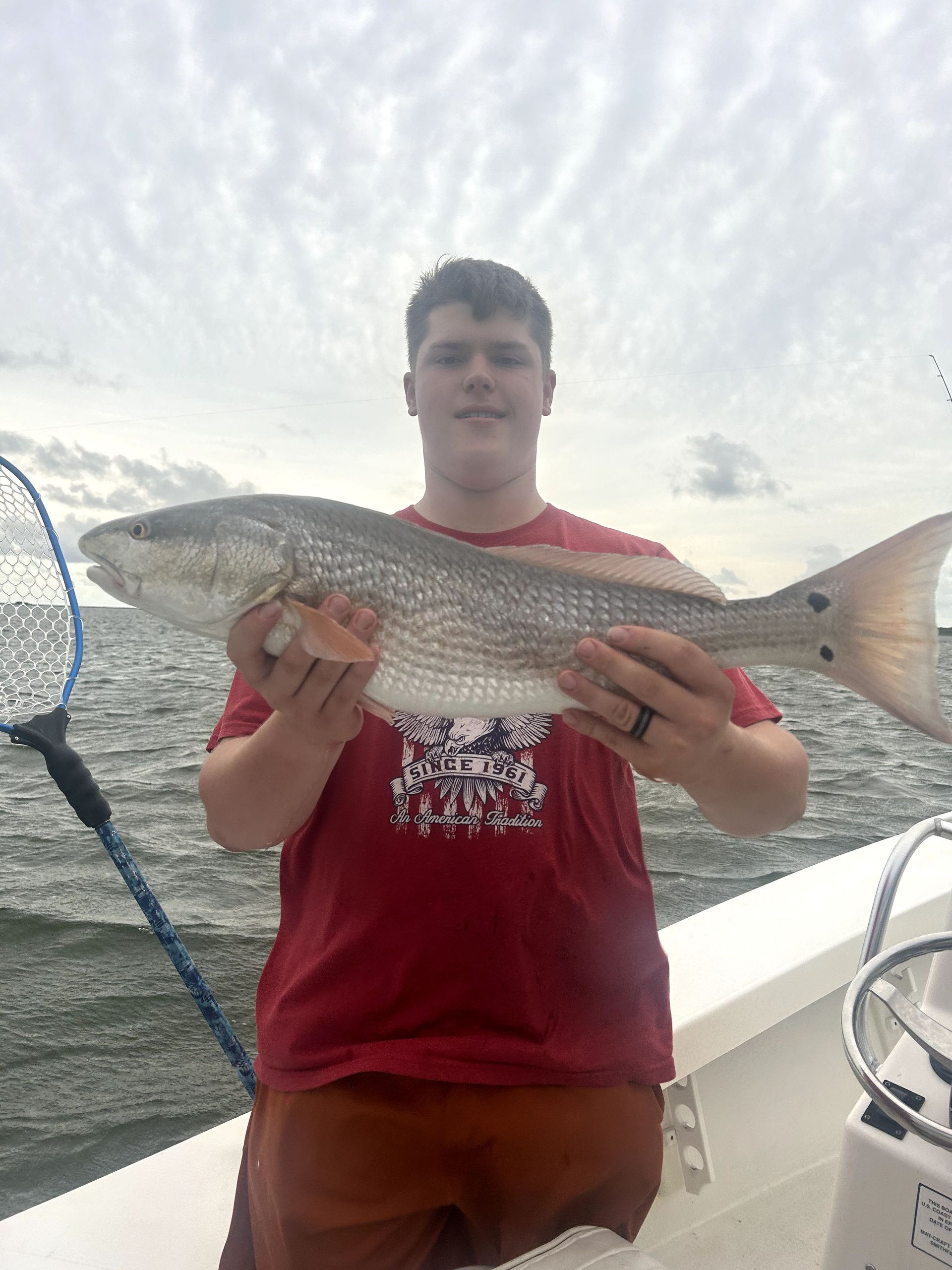 Person on a boat holding a large speckled fish over the water.