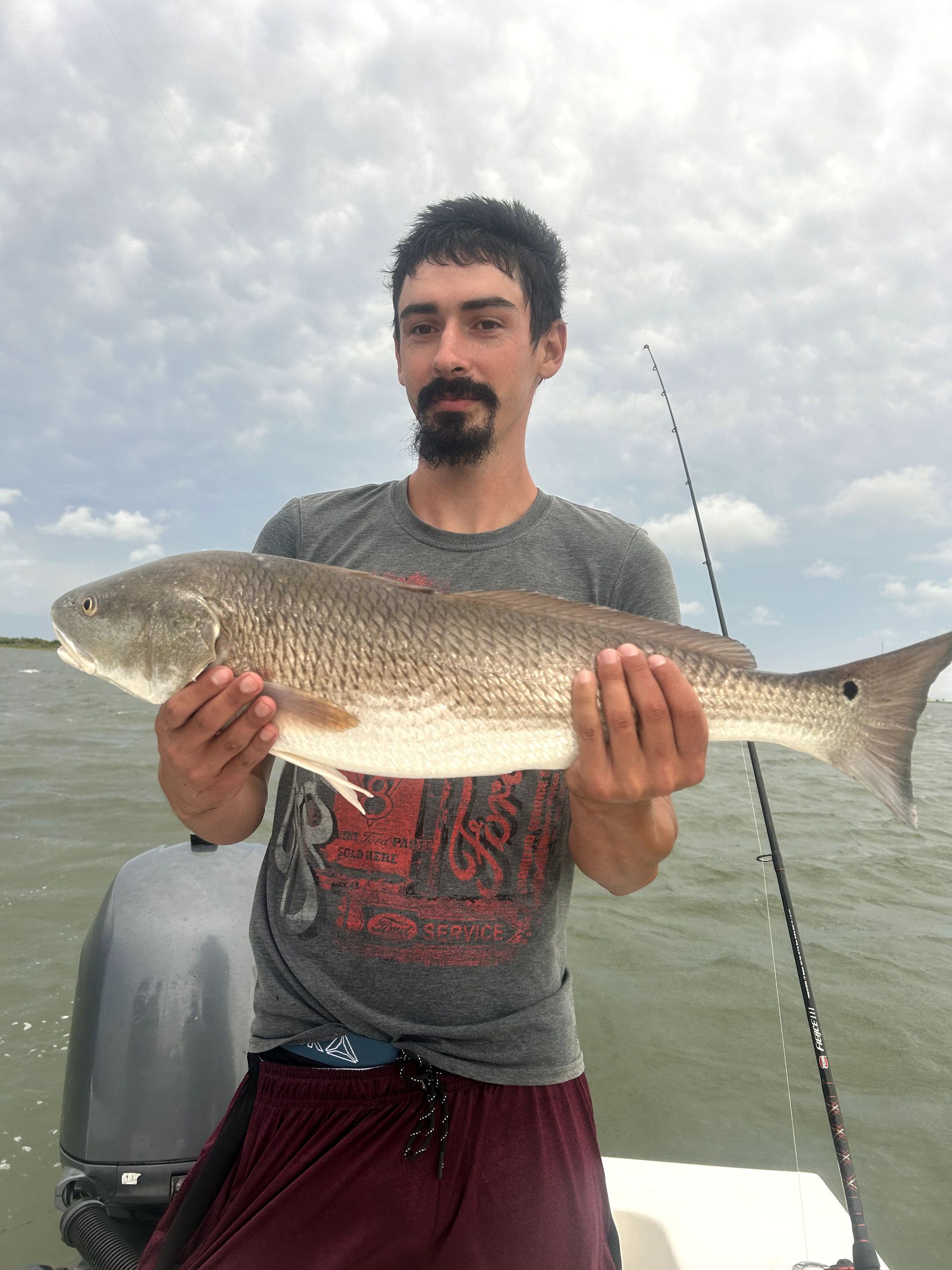 Man holding a large fish on a boat, with water and cloudy sky in the background.
