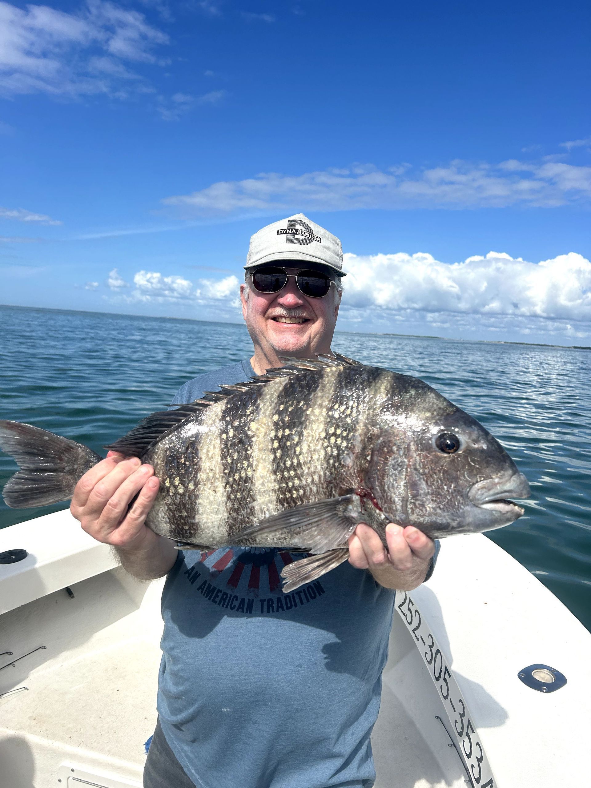 Man holding a striped fish on a boat under a bright blue sky