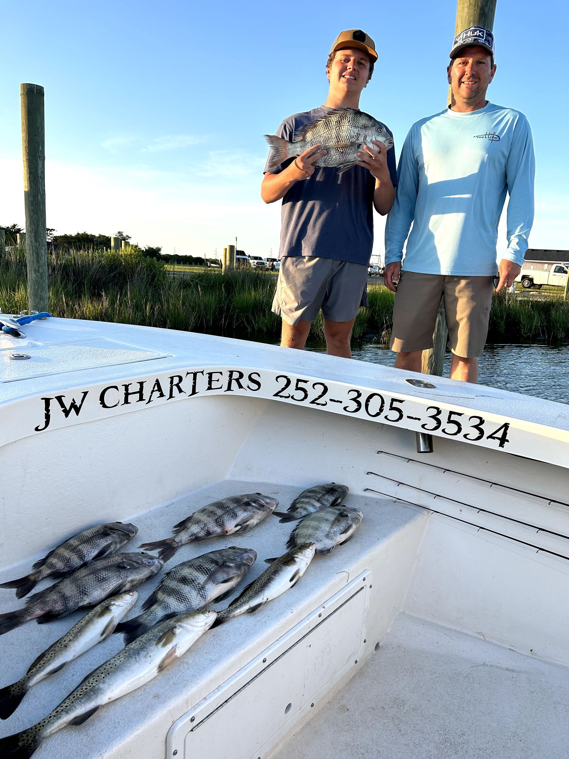 Two anglers standing on a boat with several fish in the foreground at sunset, JW Charters logo visible