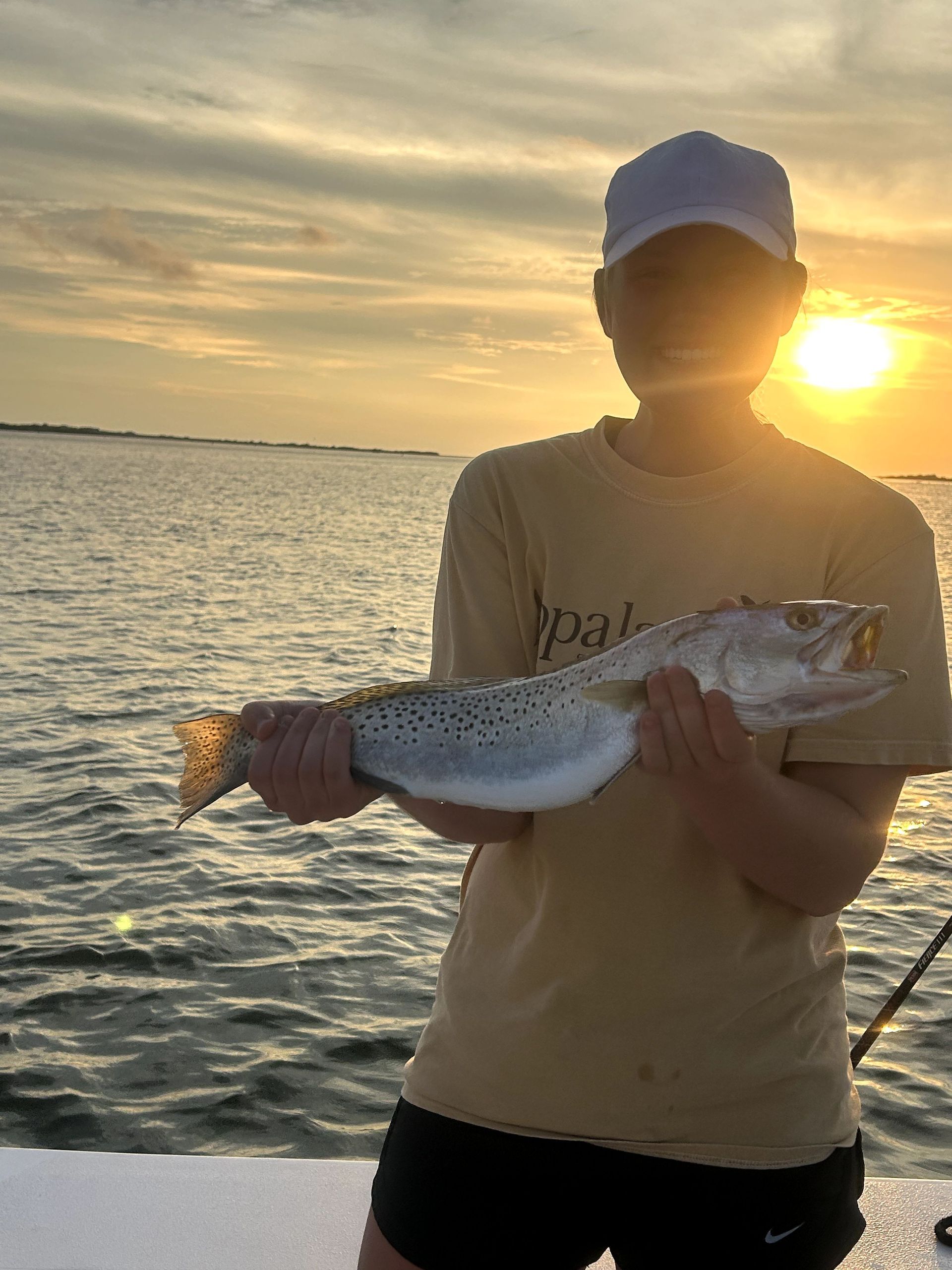 Person holding a fish at sunset on a boat, with calm water and golden sky in the background