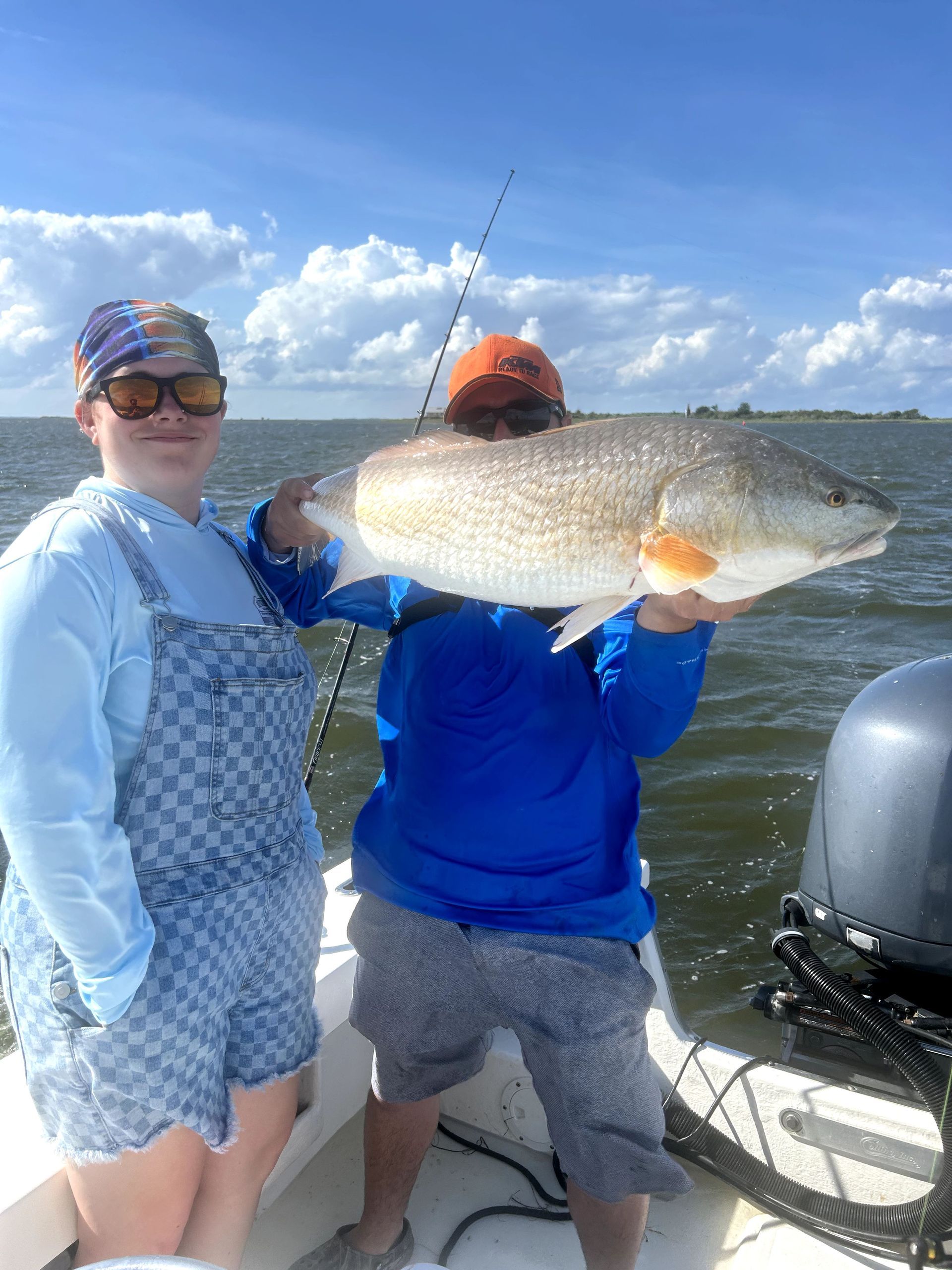 Two people on a boat holding a large fish, with water and a blue sky in the background.