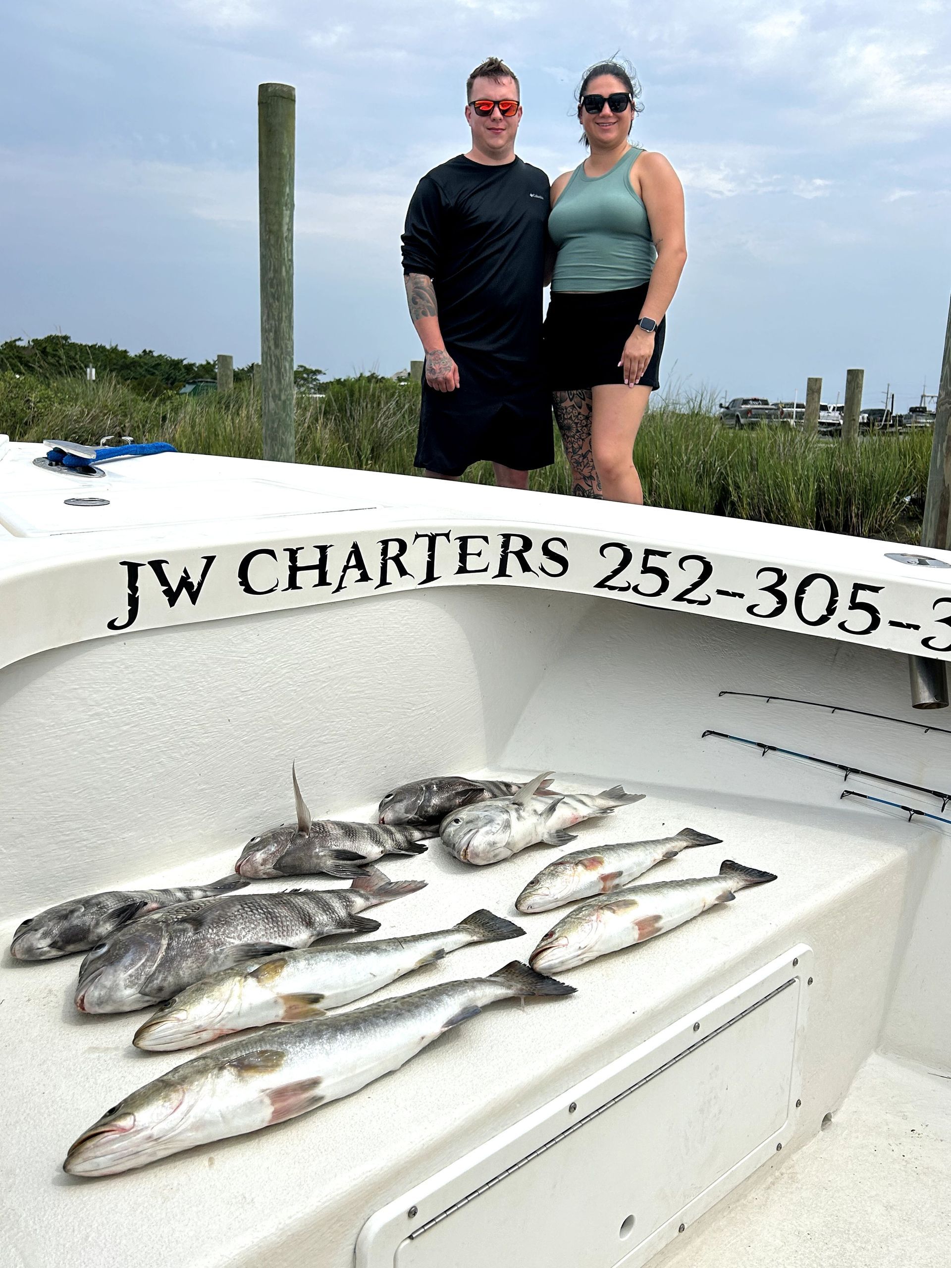 Two people on a boat with a catch of fish laid out on deck.