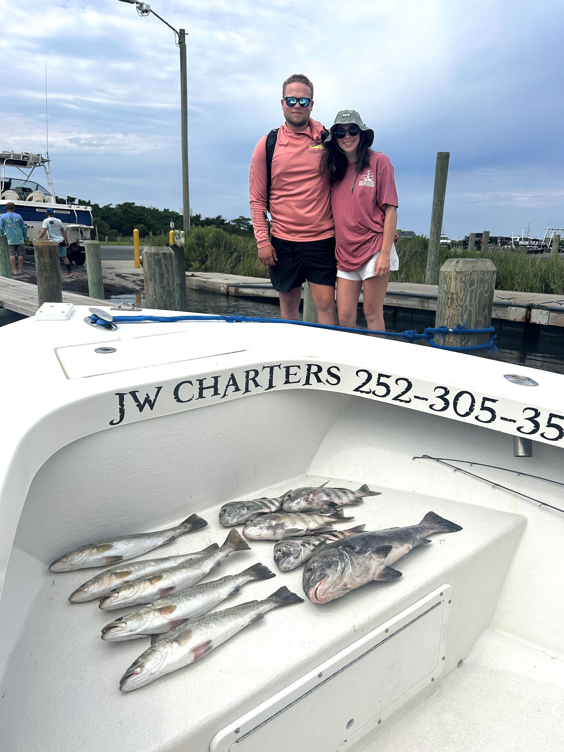 Two people on a charter boat holding fish in a dockside harbor setting