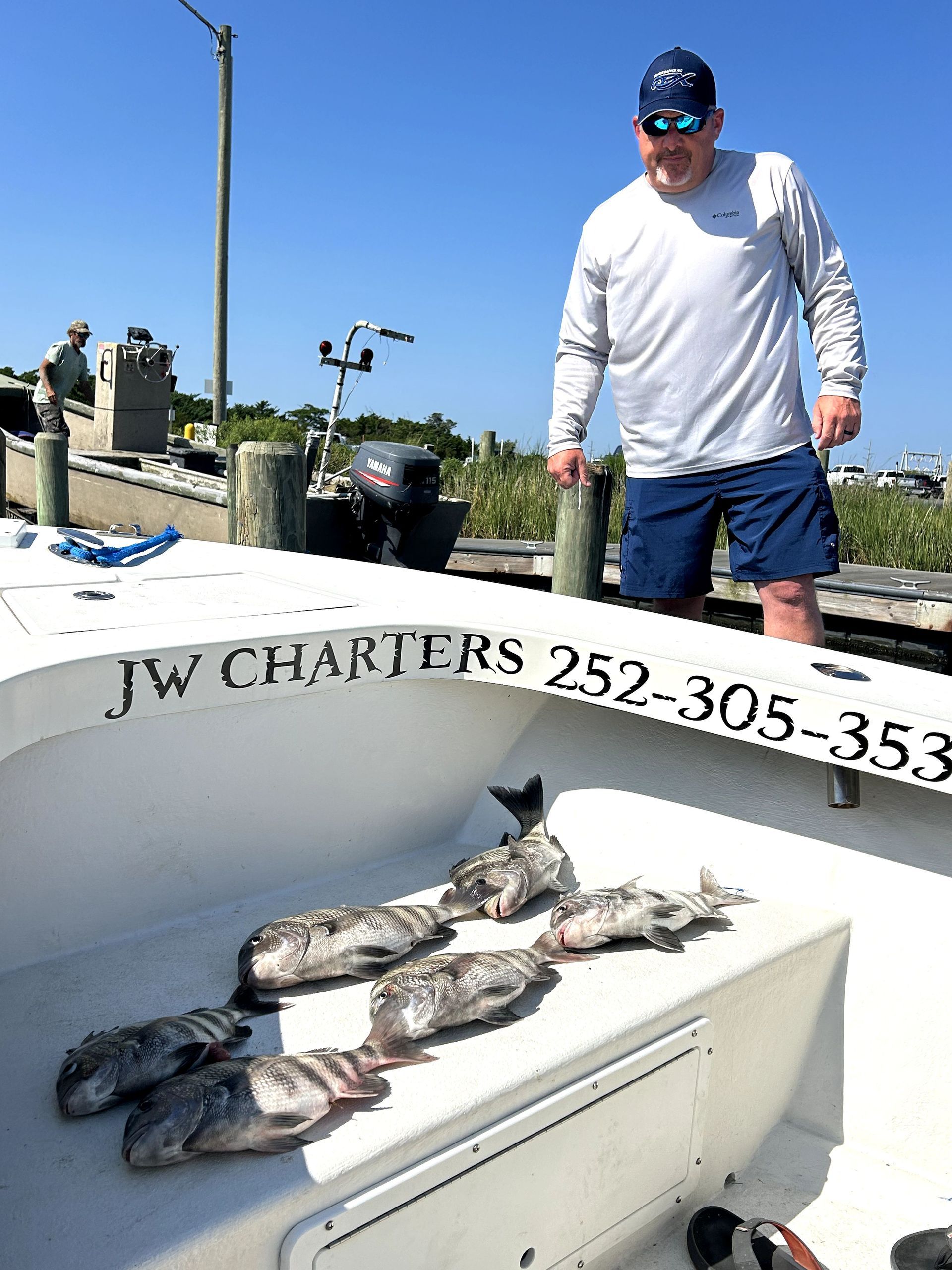 Man on a boat with several fish laid out on deck under a blue sky.