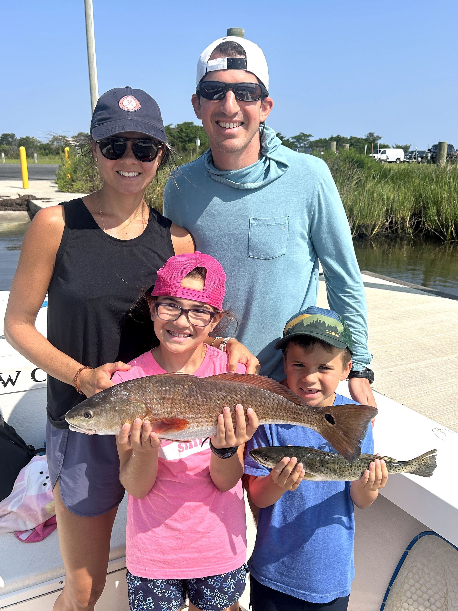 Family on a boat holding two large fish, smiling outdoors on a sunny day.