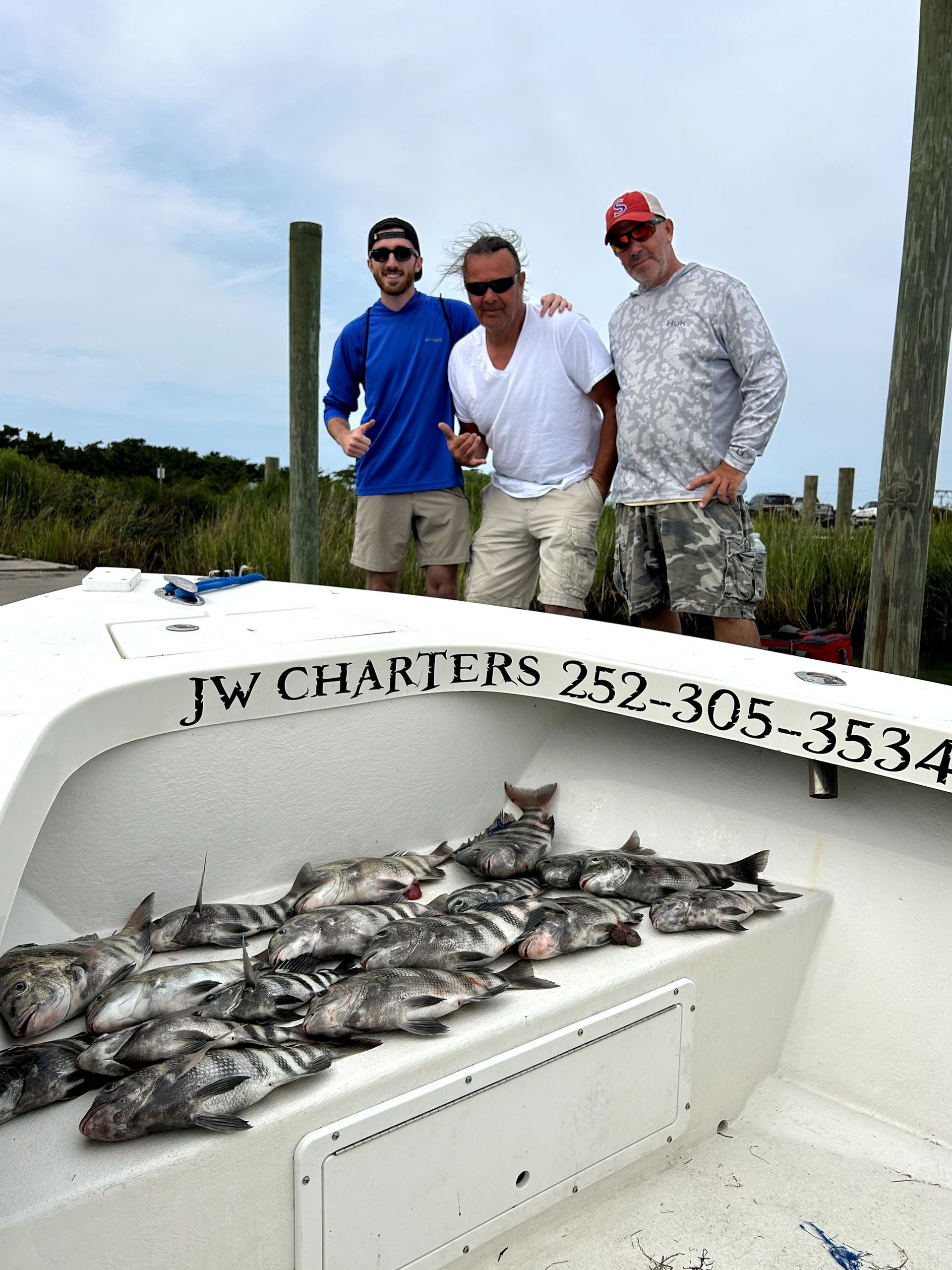 Three anglers on a charter boat pose behind a pile of caught fish.