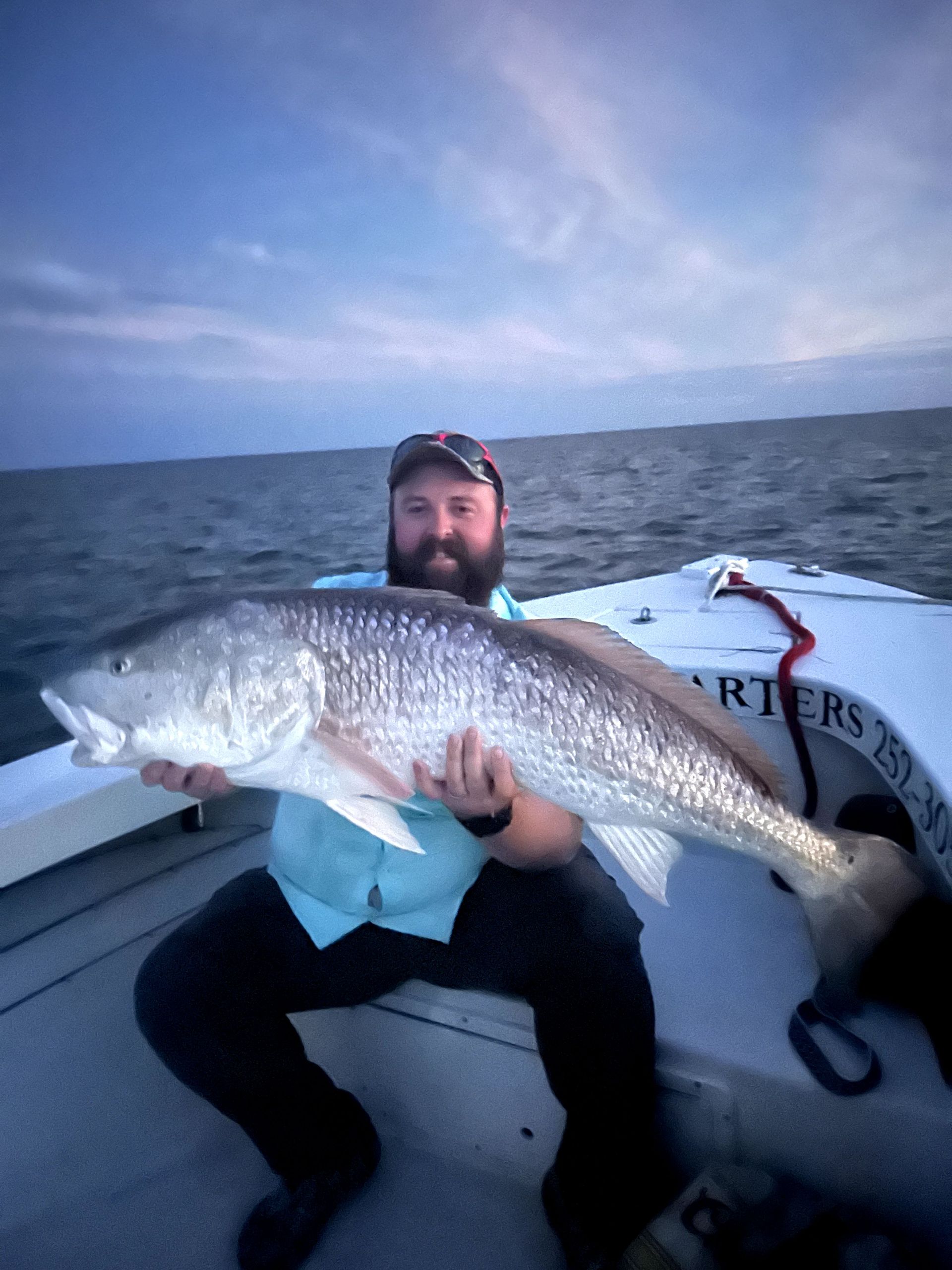 Man on a boat holding a large silver fish on a cloudy ocean