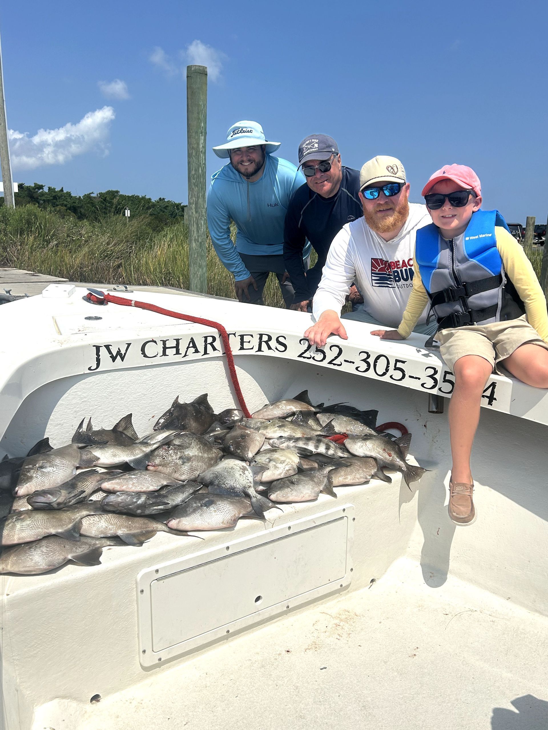 Four people on a boat hold a large catch of fish on a sunny day.