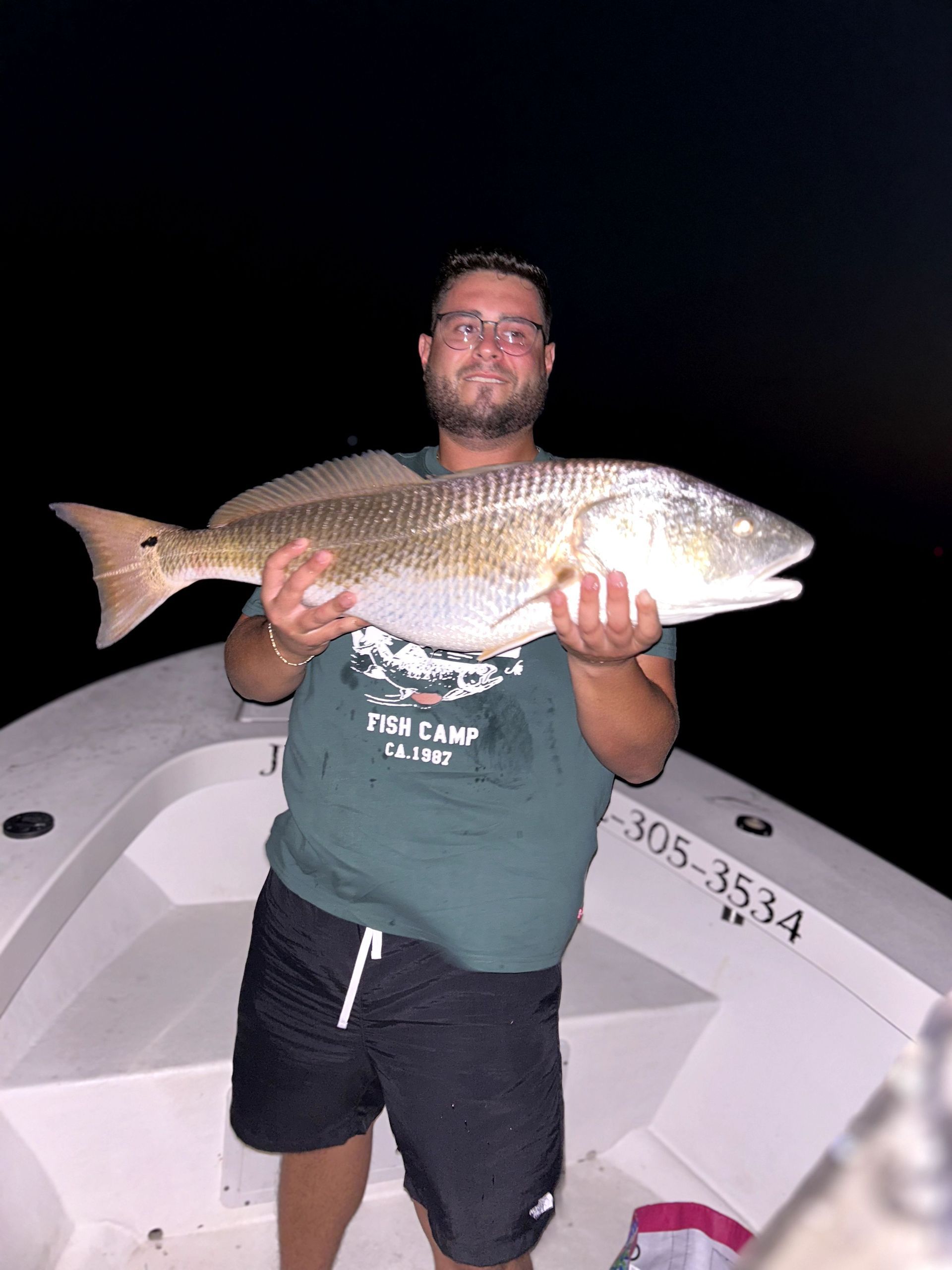 Man holding a large fish on a boat at night