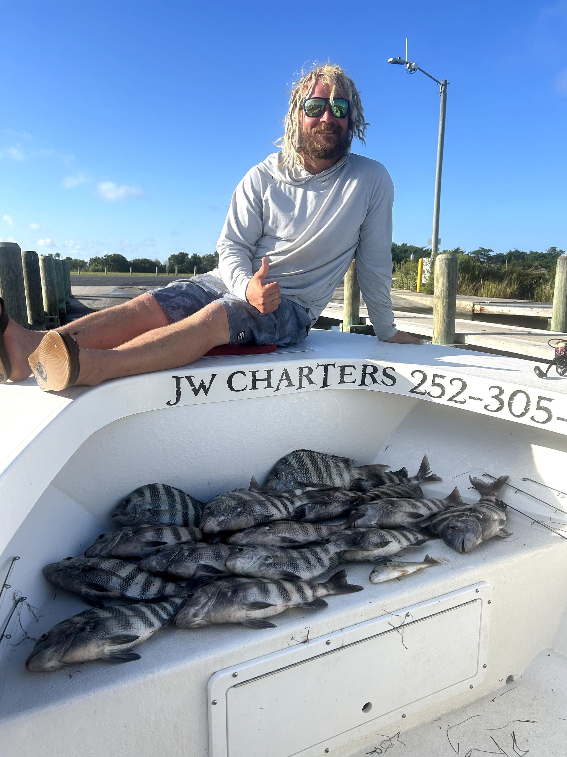 Person sitting on a boat with a large catch of fish in a built-in cooler, under a sunny blue sky.