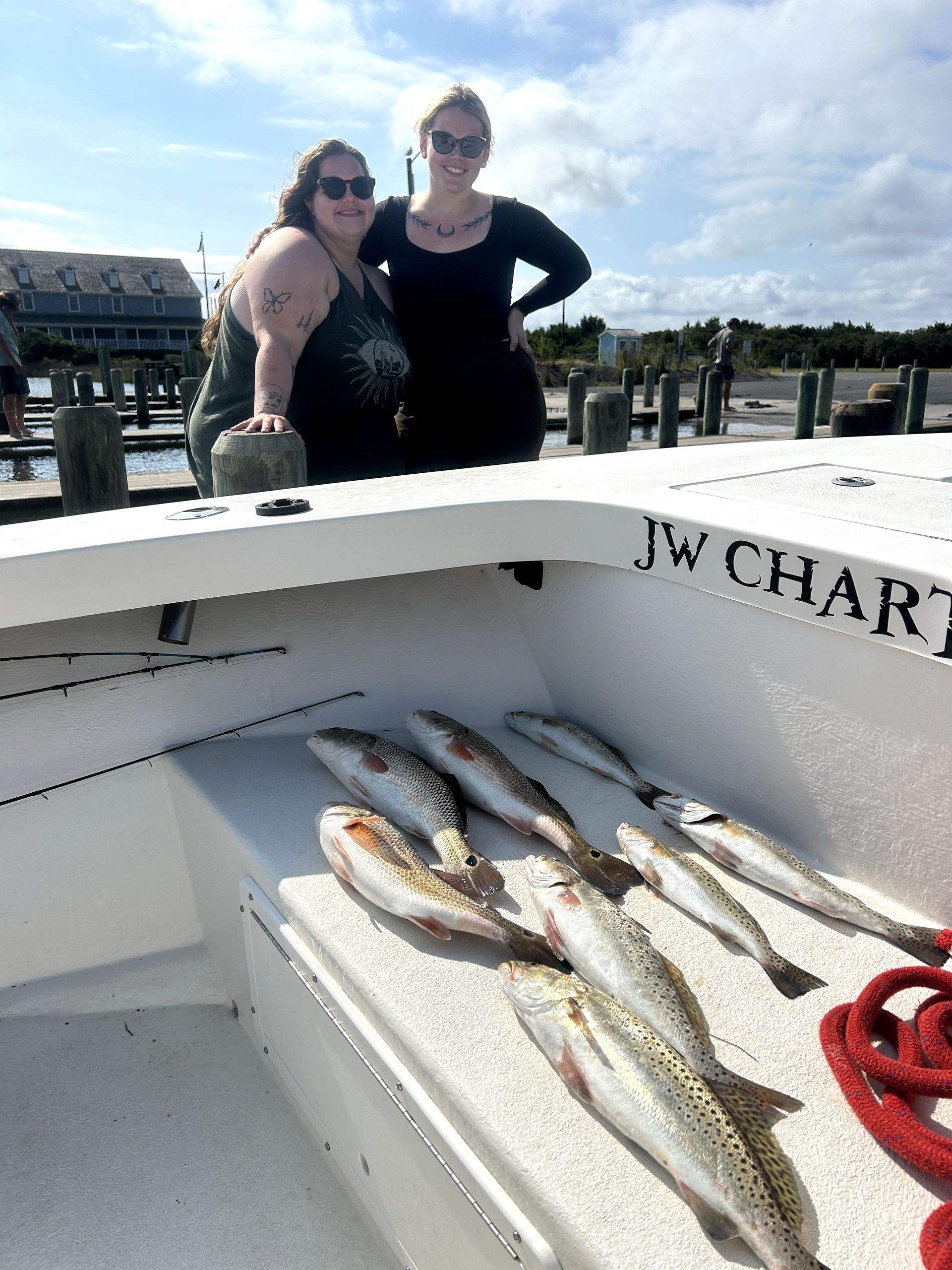 Two people on a boat with several fish laid out in the foreground, dock and water behind them.