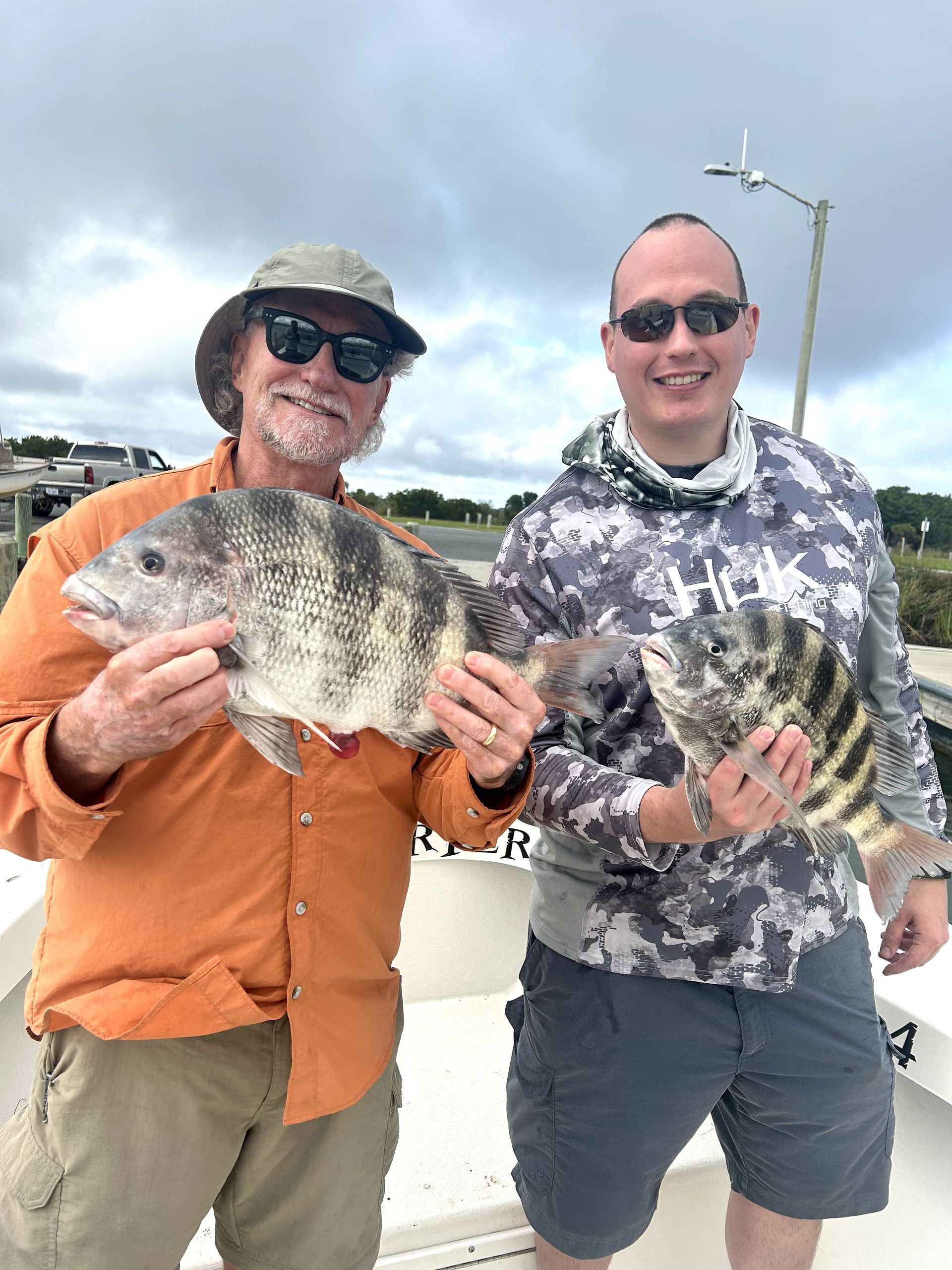 Two people on a beach holding up fish and smiling at the camera.