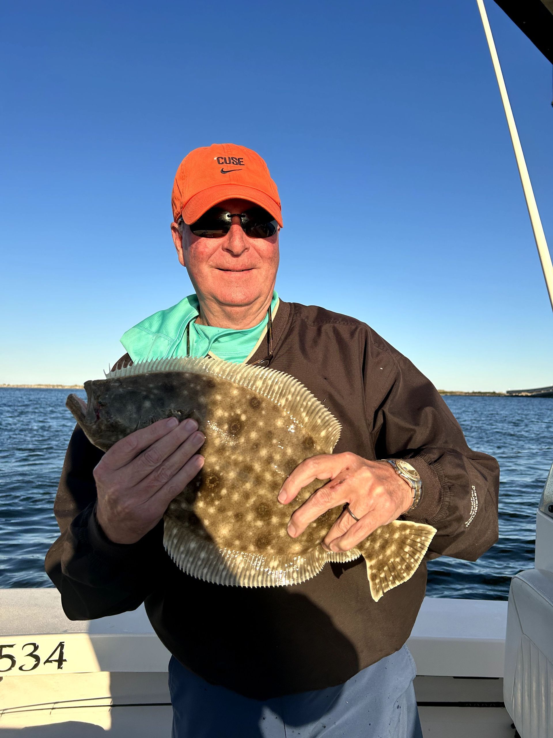 Person holding a large flat fish on a boat, wearing an orange cap and dark sunglasses.