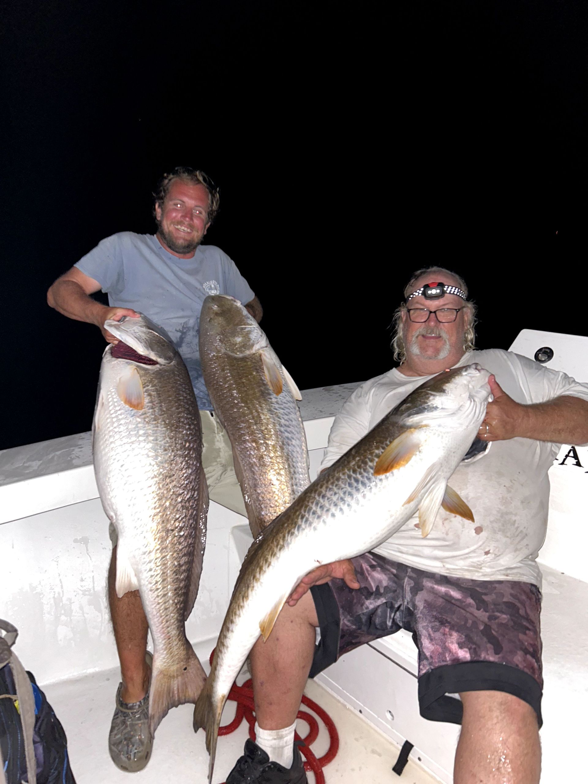 Two people on a boat at night holding large fish they just caught