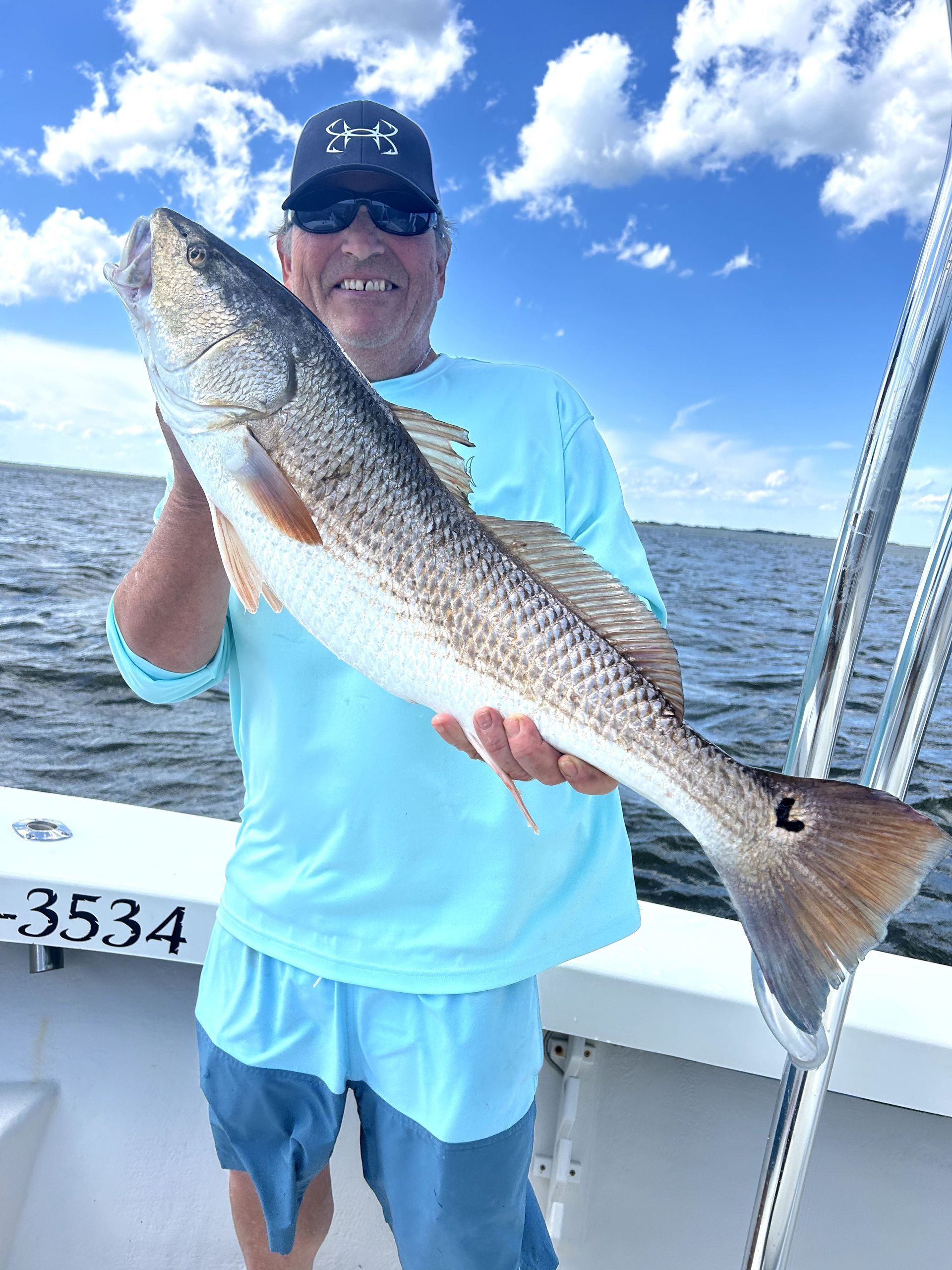Man holding a large fish on a boat under a blue, cloudy sky