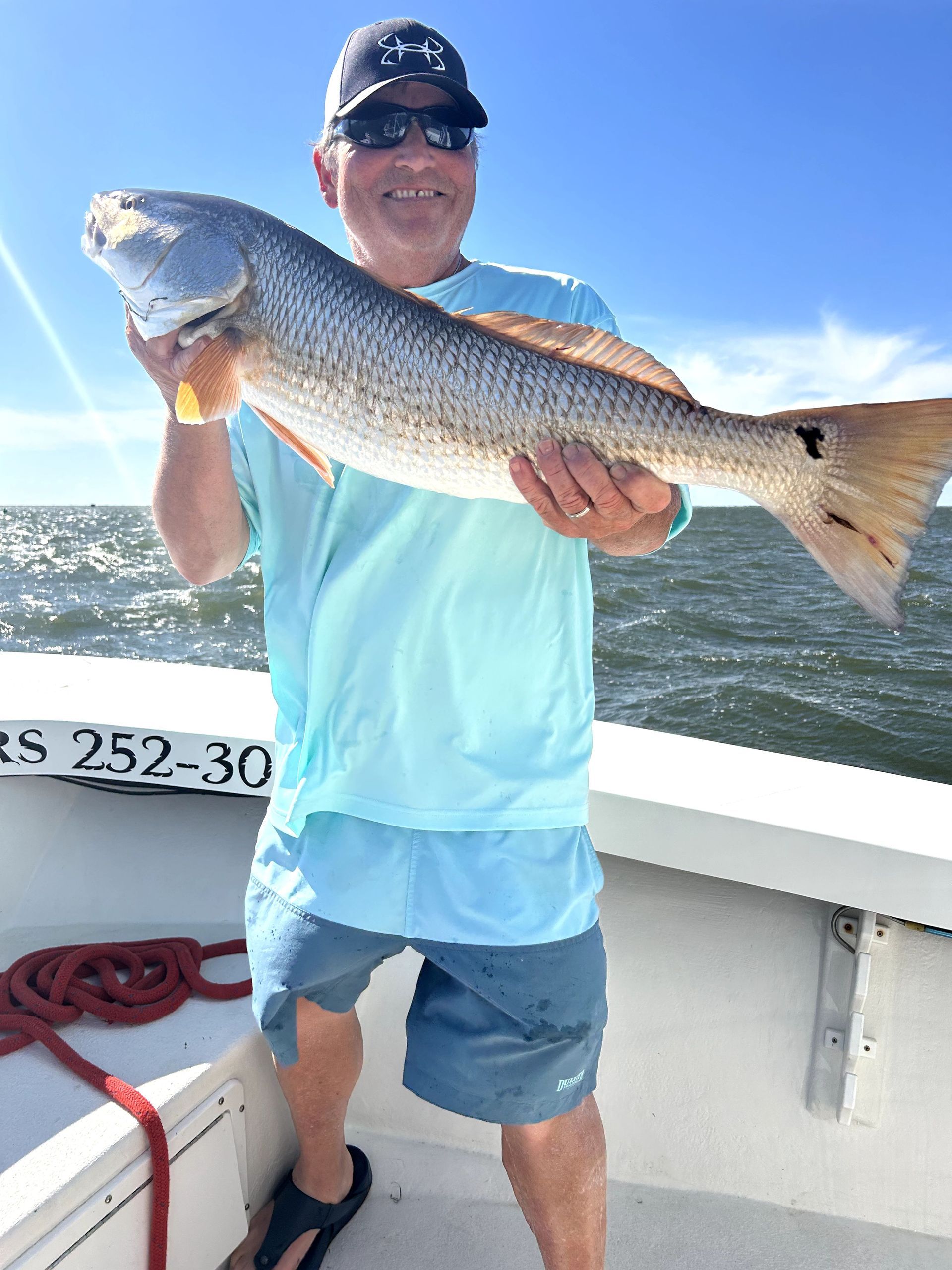 Person on a boat holding a large fish on a sunny day.
