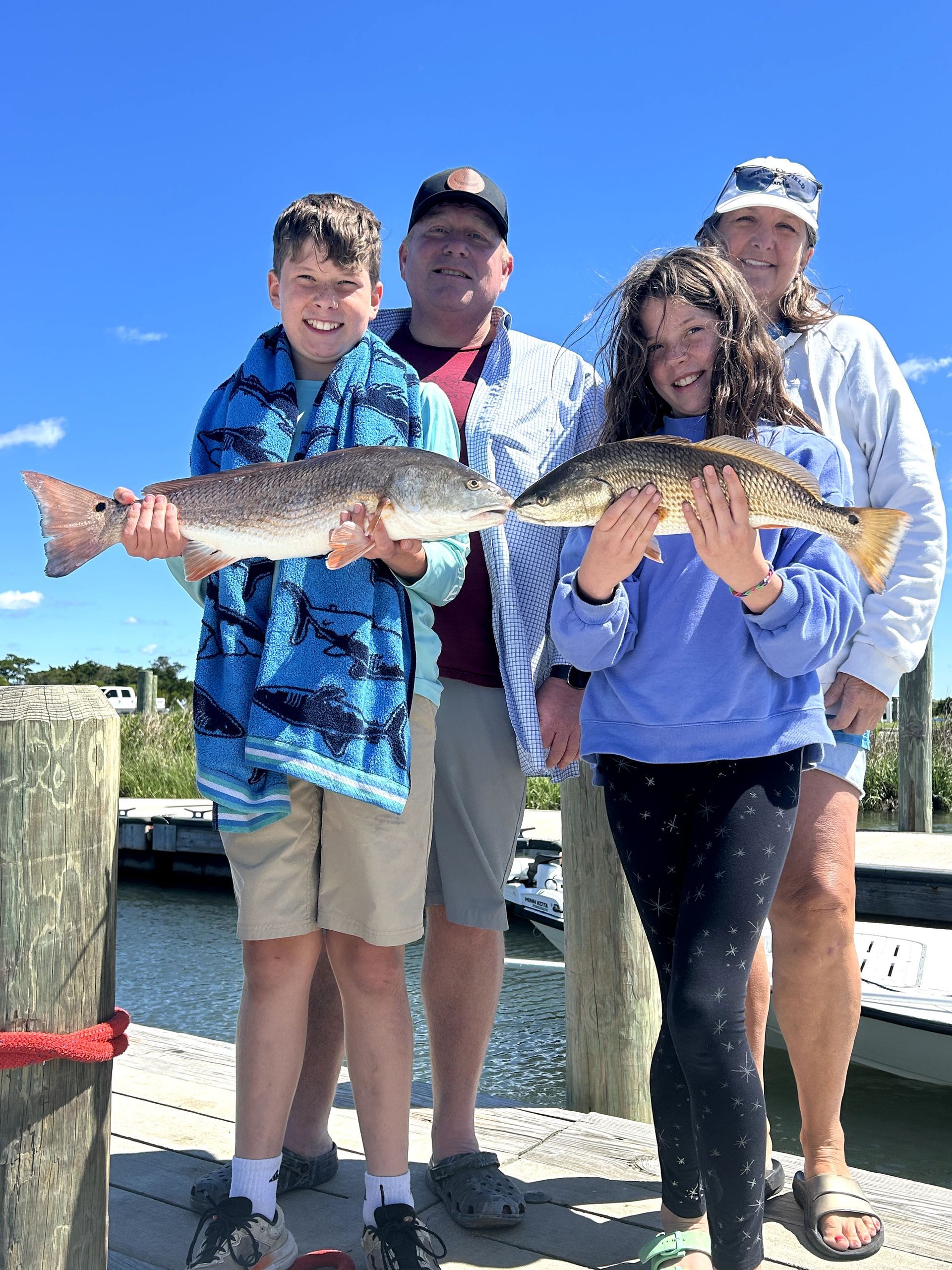 Four people holding a large fish on a sunny dock by the water