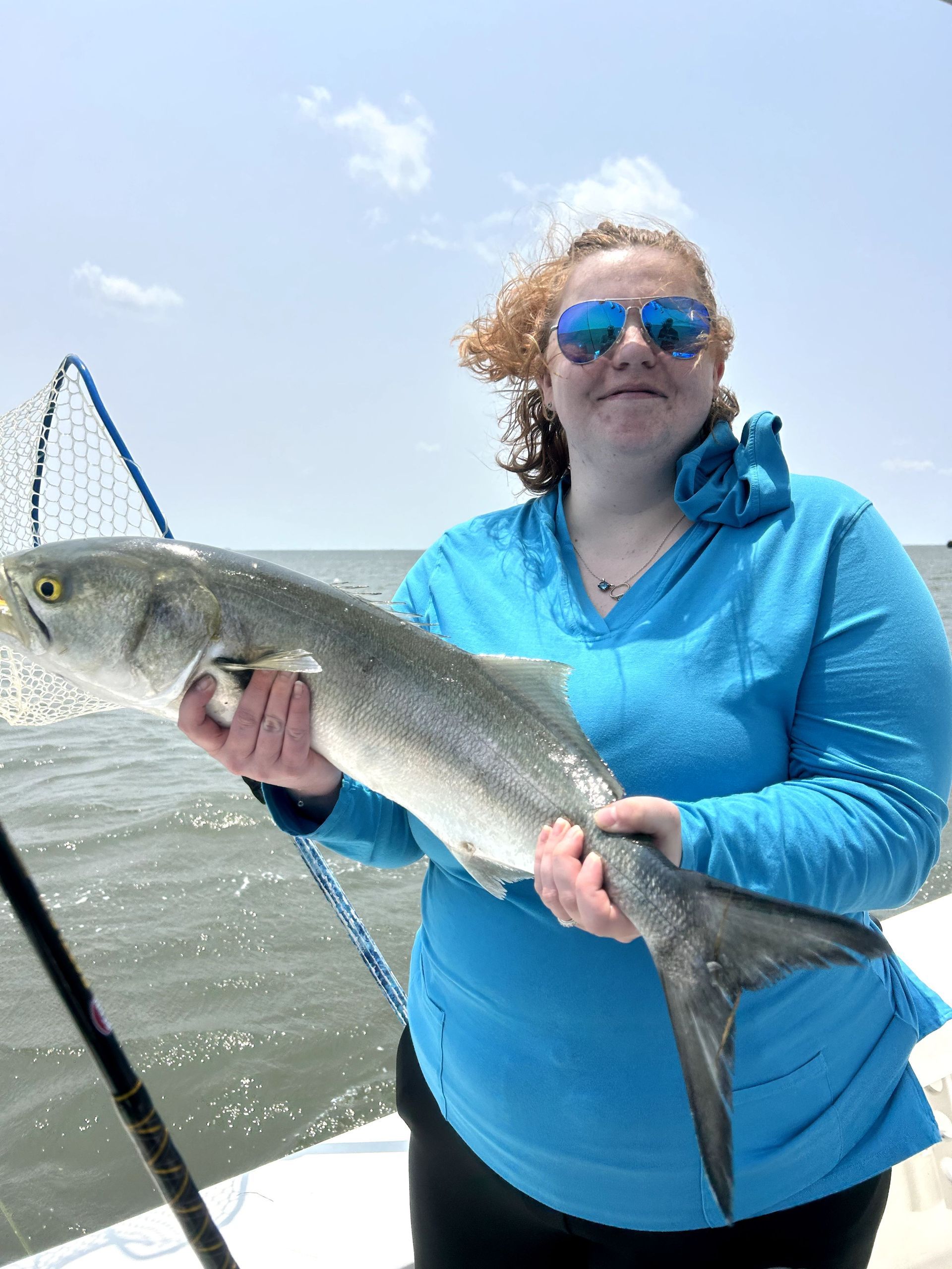 Person in blue shirt holding a large silver fish on a boat under a bright sky.