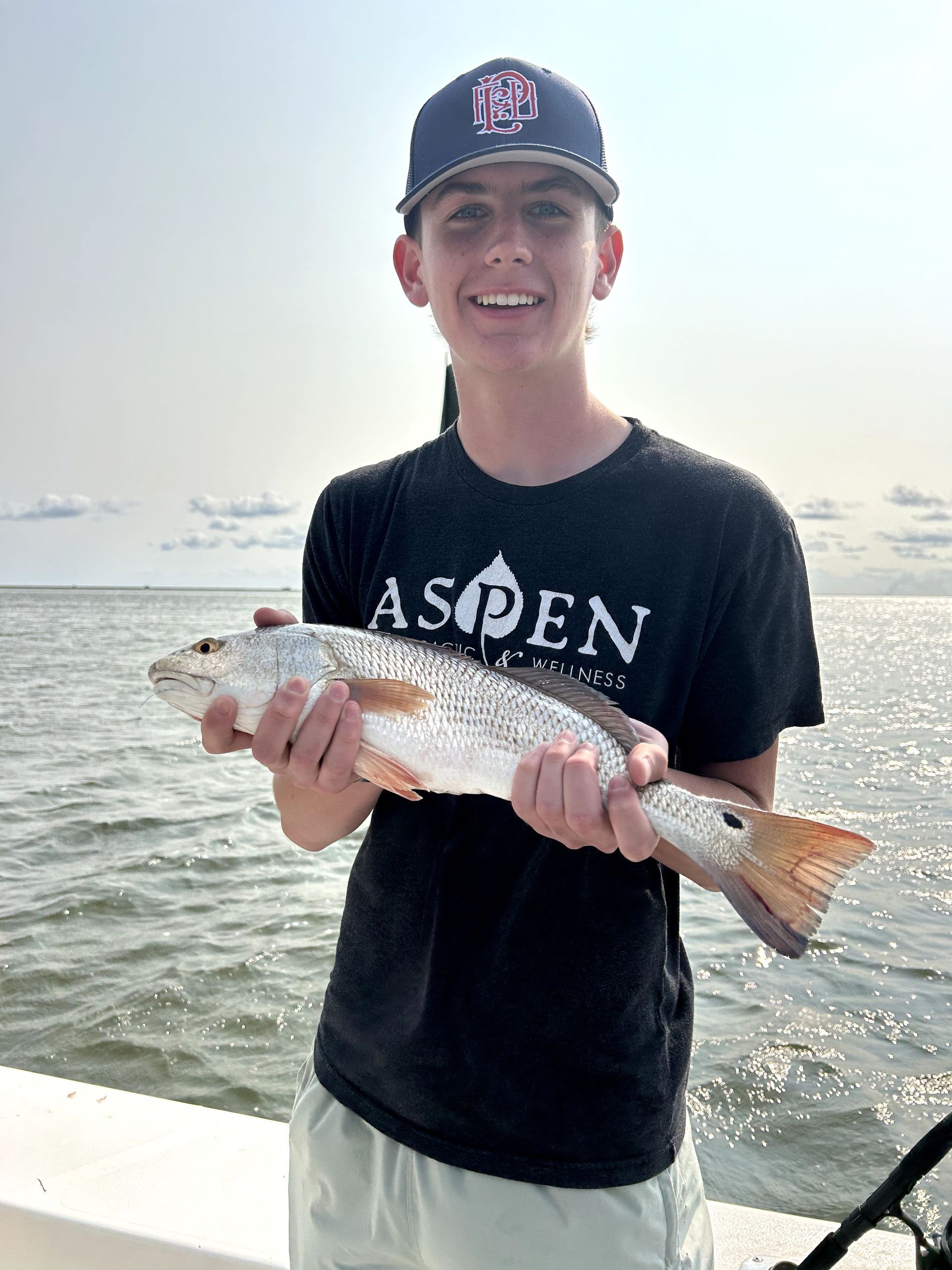 Person holding a large fish on a boat with water and ships in the background