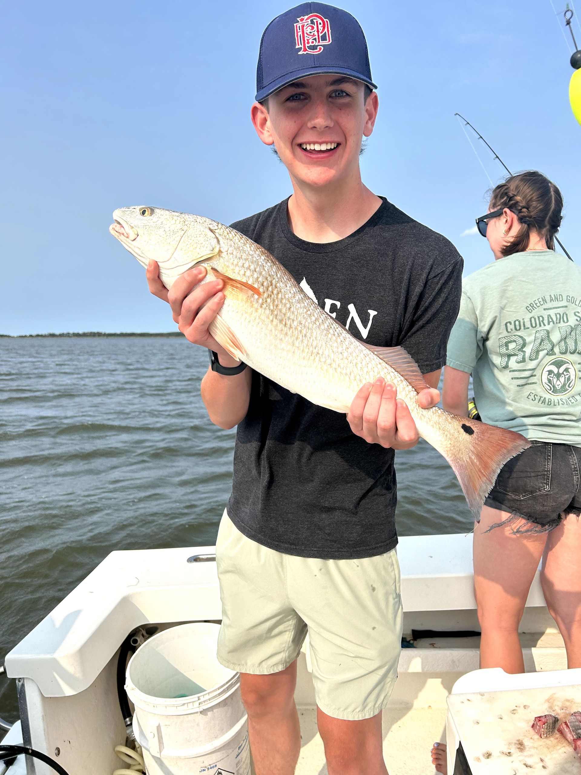 Person on a boat holding a large fish, smiling on a sunny day on the water.