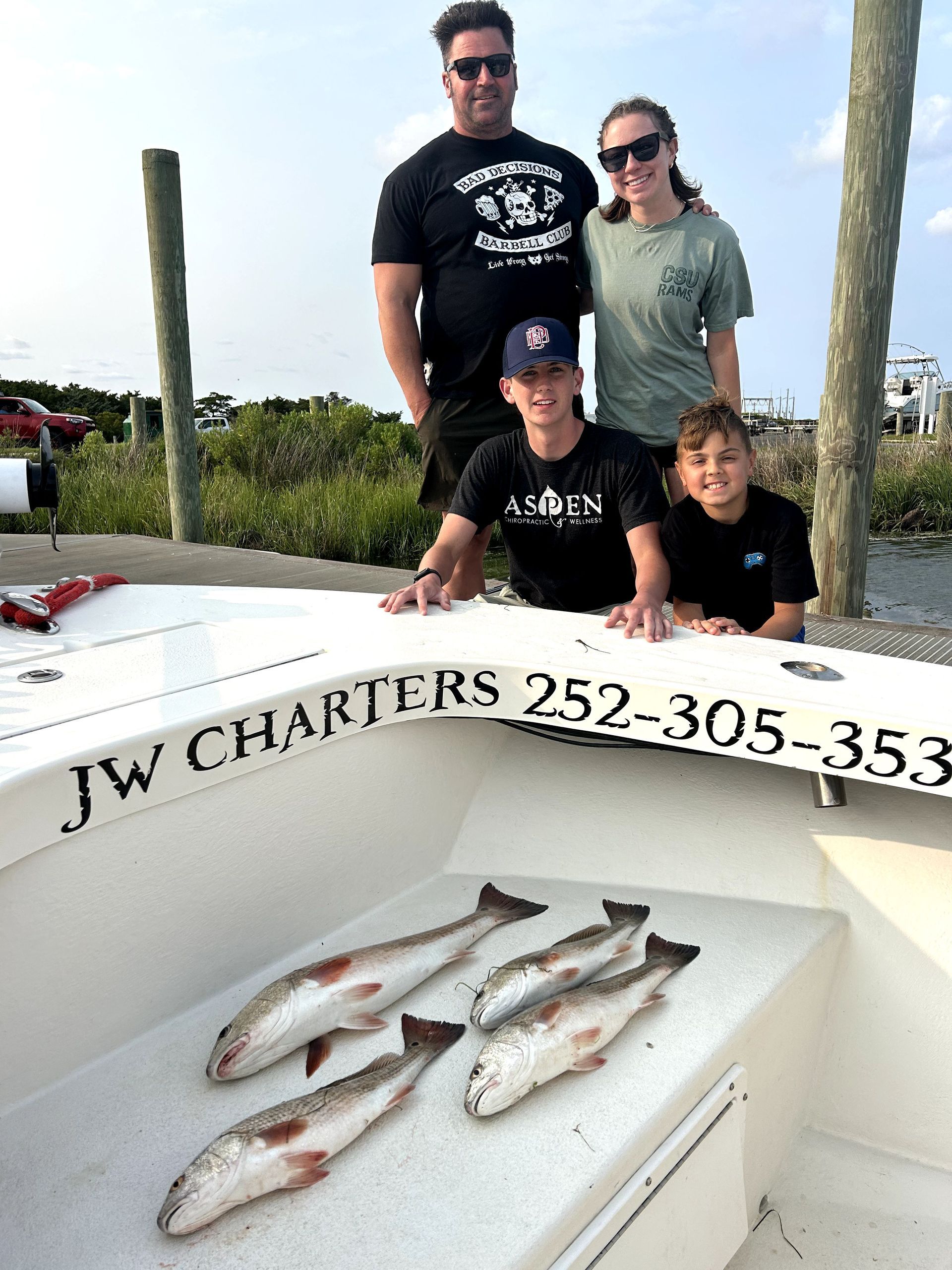 Four people posing by a boat with several fish laid out on the deck.