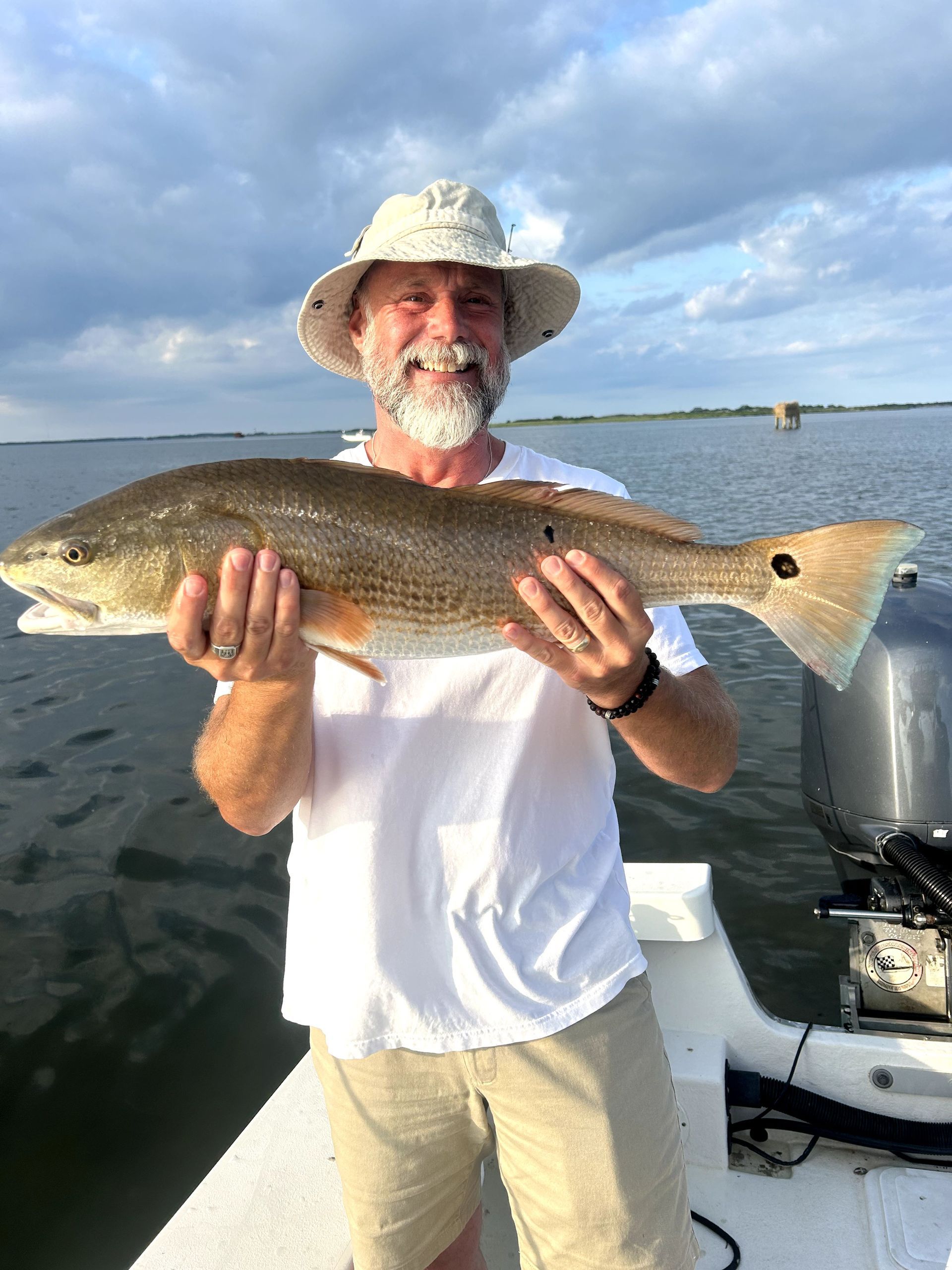 Man holding a large fish on a boat, with calm water and cloudy sky in the background