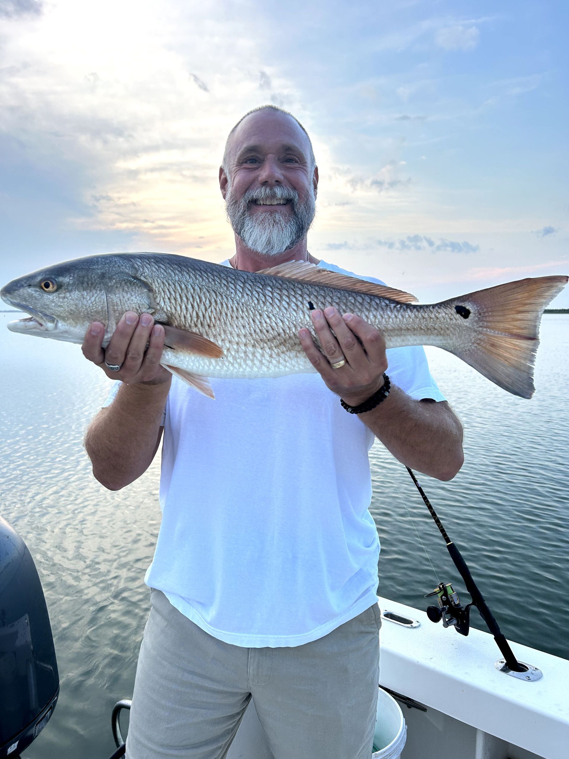Man on a boat holding a large silver fish over calm water at sunset