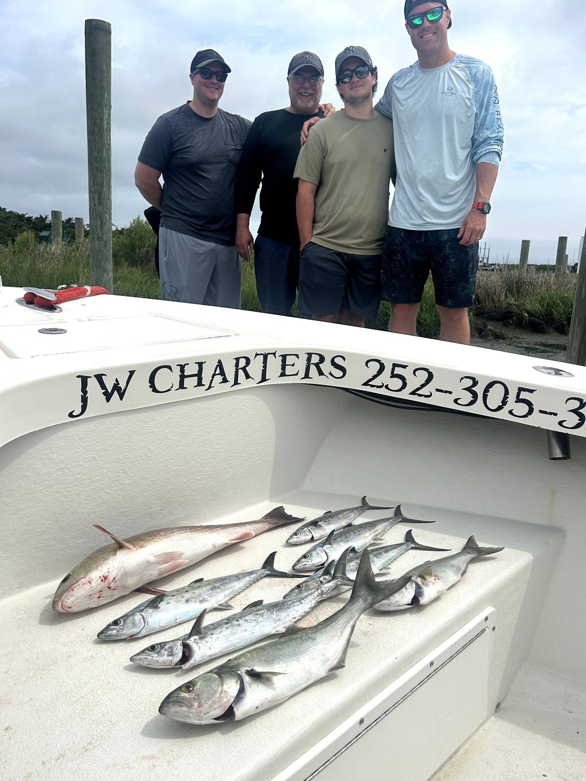 Four men stand on a boat with a catch of fish laid out on the deck.