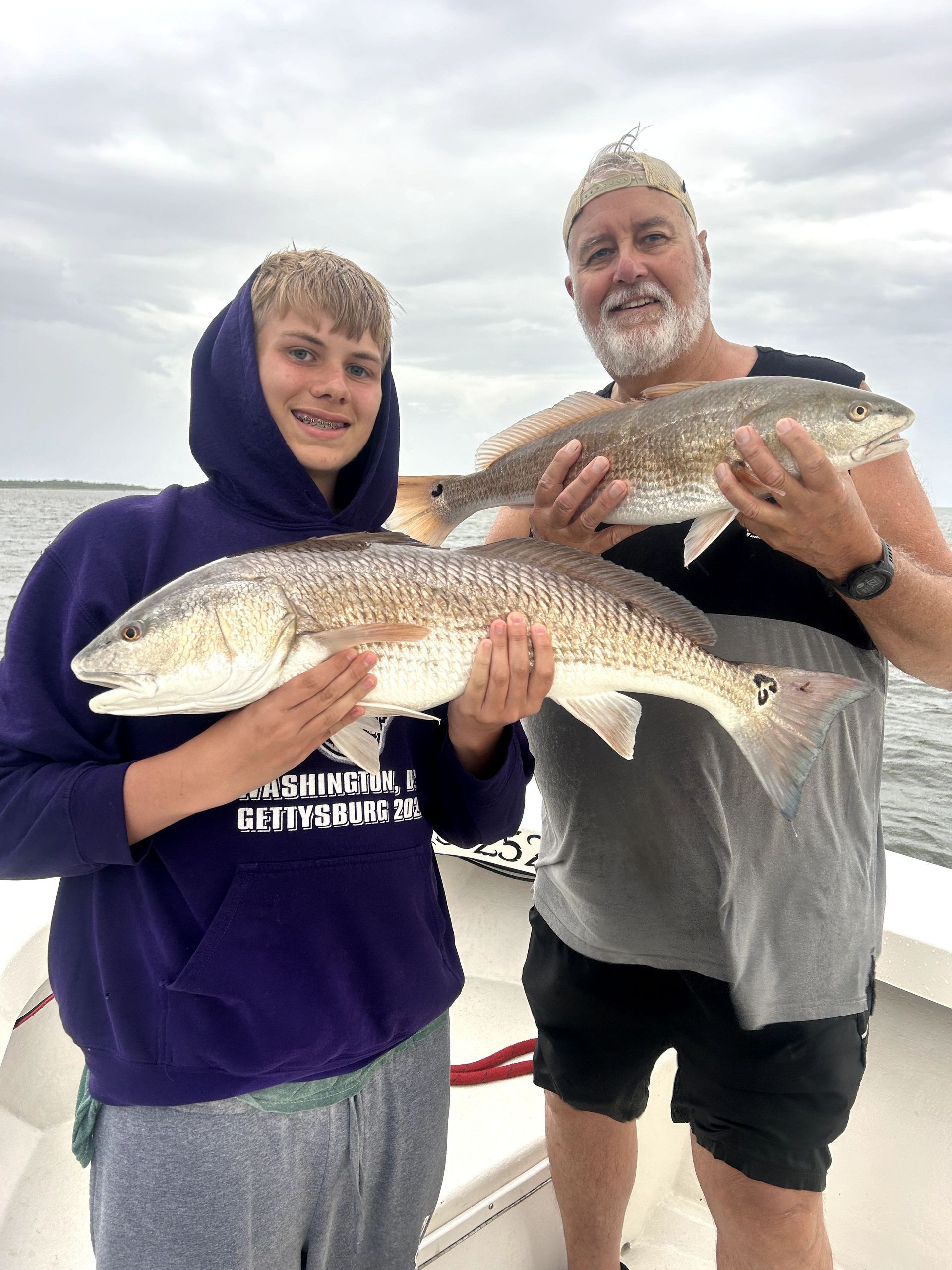 Two people on a boat holding large fish against a cloudy sky.