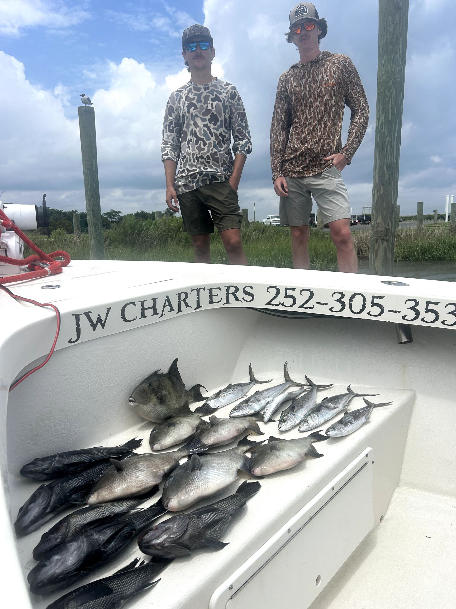Two anglers on a boat with a large catch of fish displayed in a white cooler