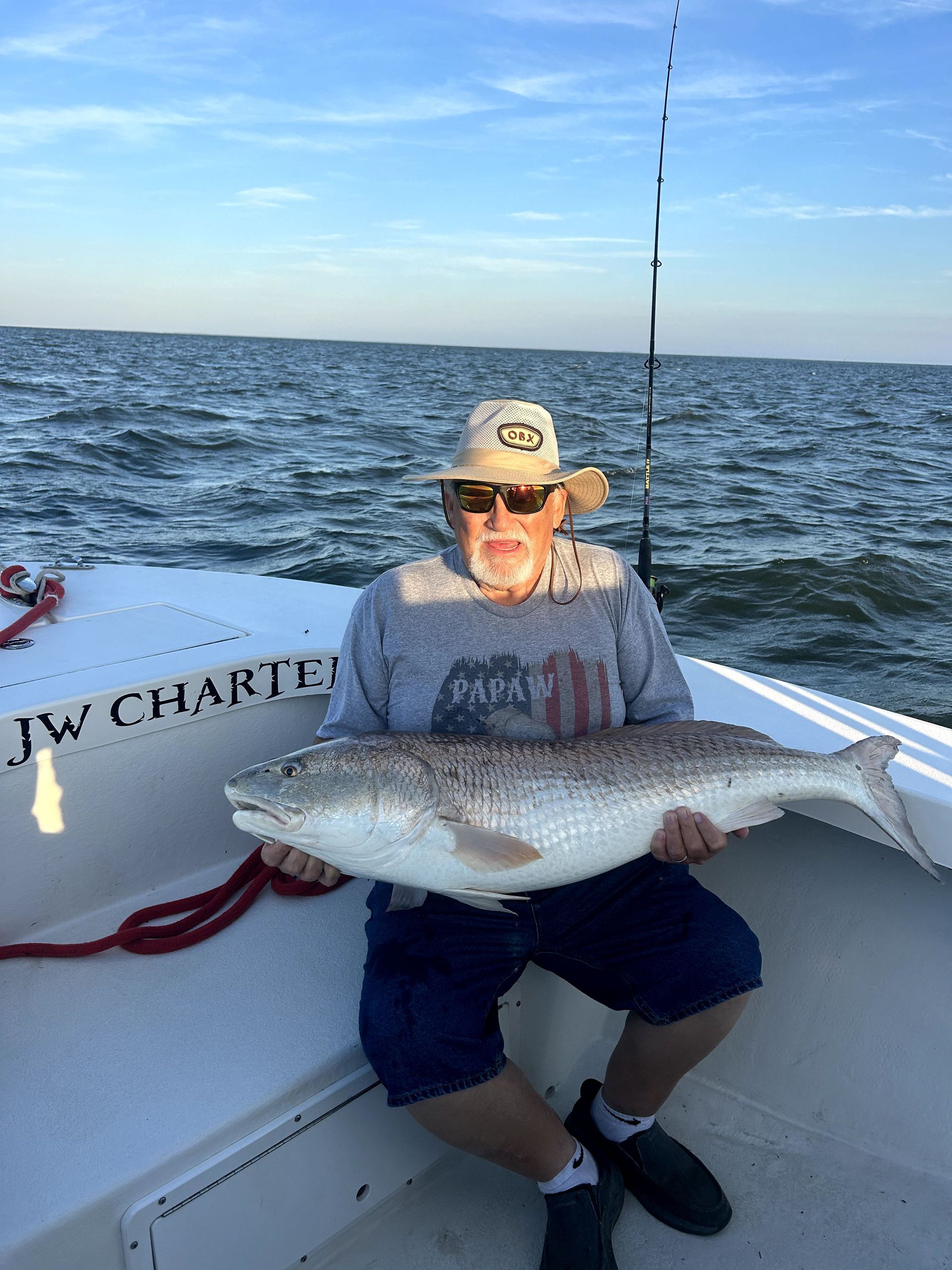 Man on a fishing boat holding a large silver fish on open water under a clear sky