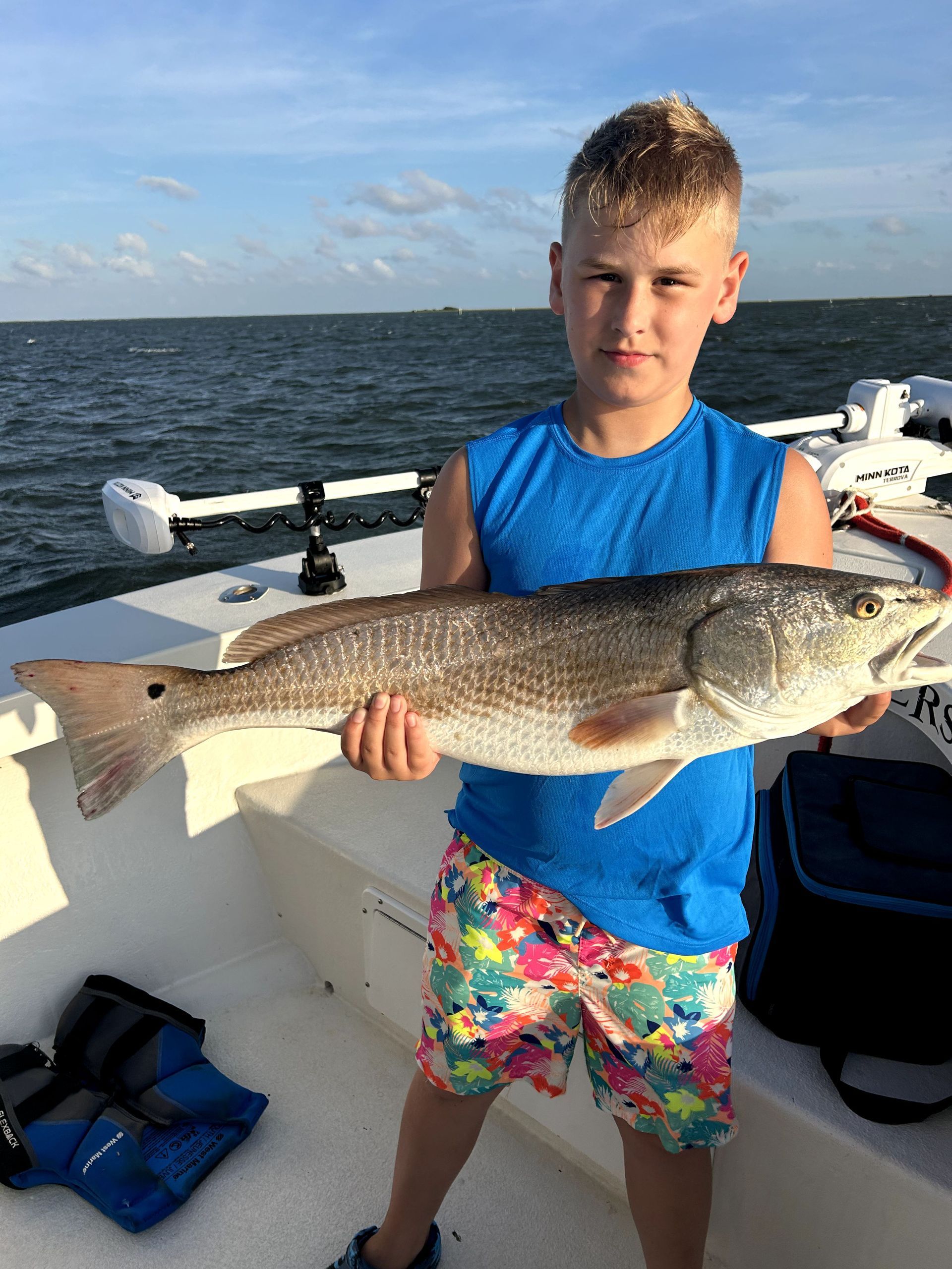 Boy on a boat holding a large fish, with open water in the background.