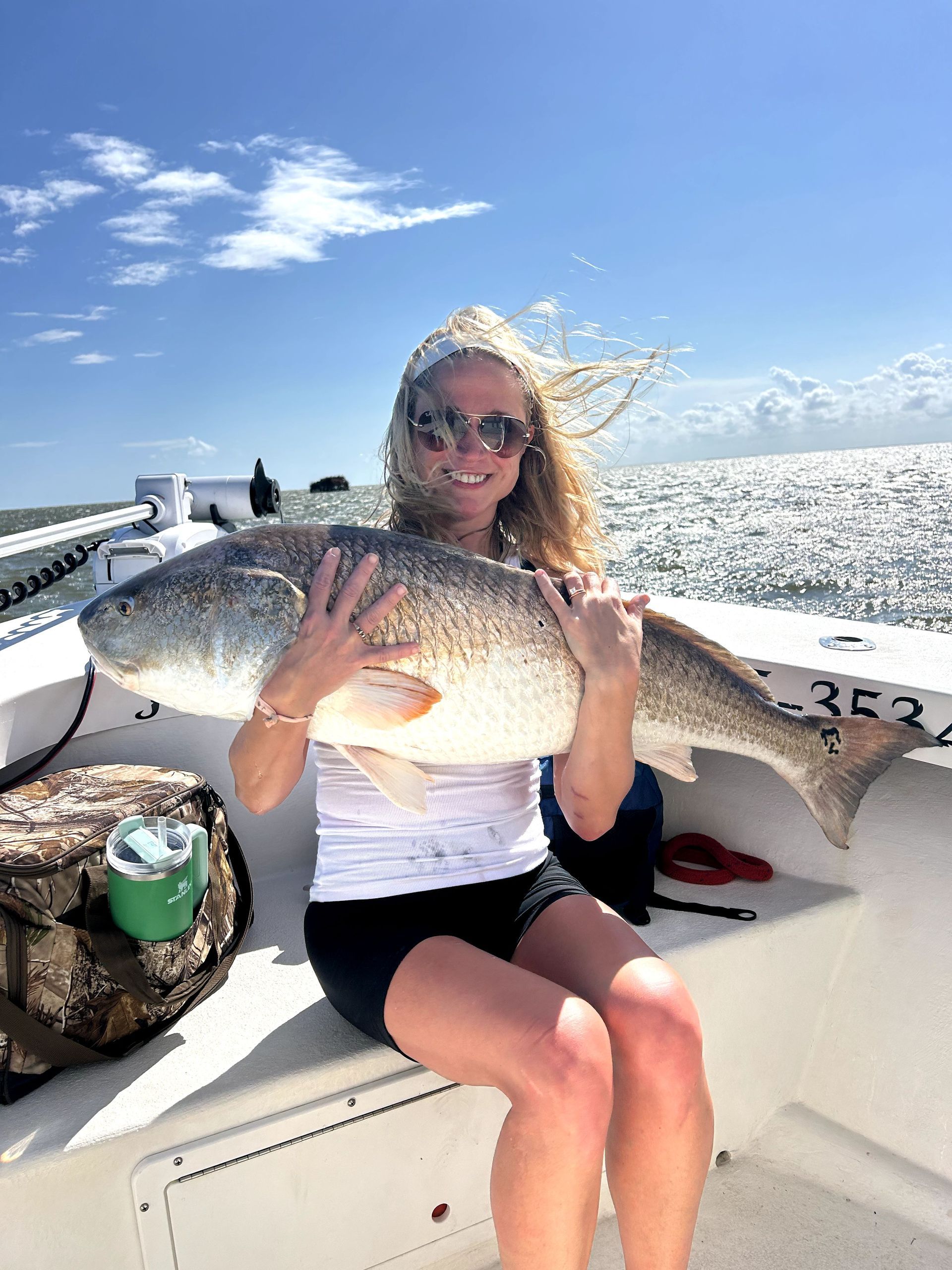 Person on a boat holding a large fish under a bright blue sky.