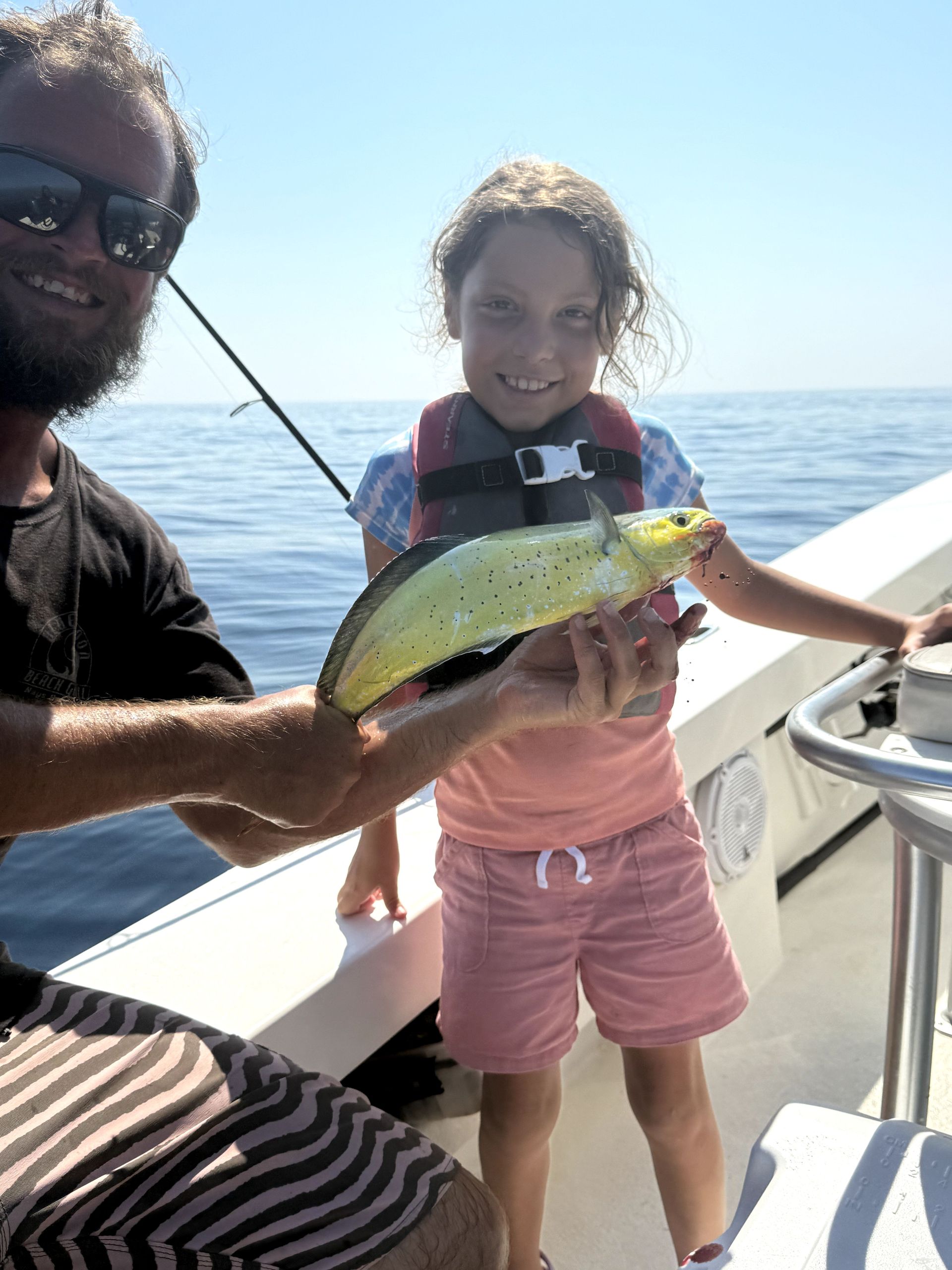 Two people on a boat holding up a yellow-green fish on a sunny day at sea