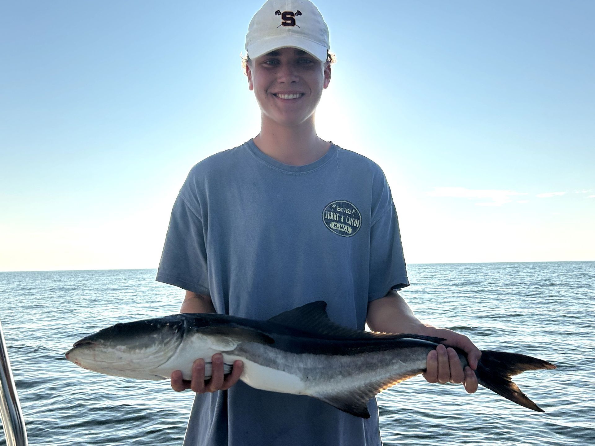 Person holding a large fish on a boat with ocean and clear sky in the background