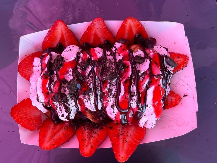 Chocolate-drizzled dessert topped with whipped cream and strawberries on a pink tray
