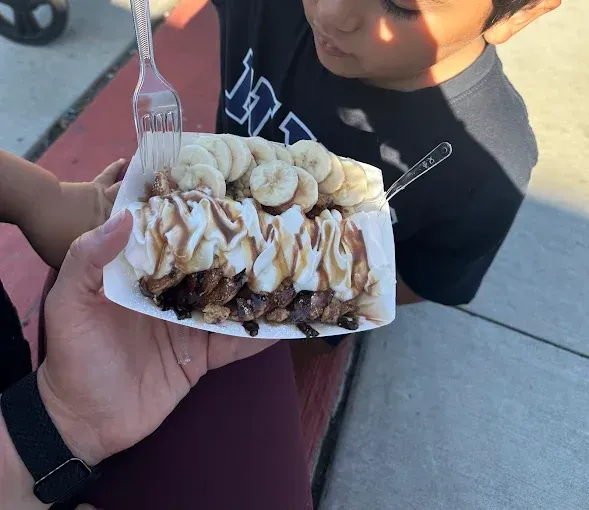 Hand holding a dessert tray topped with banana slices and whipped cream, with a child in the background